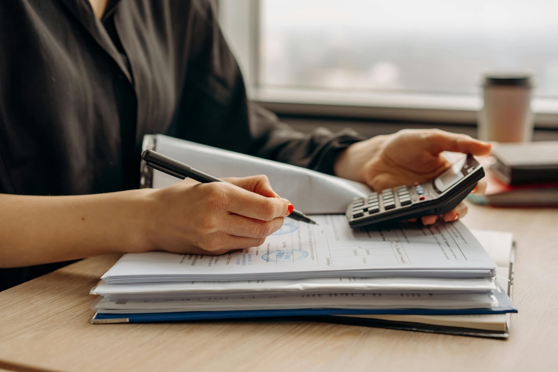 Woman writing down notes on a stack of printed reports while looking at her calculator