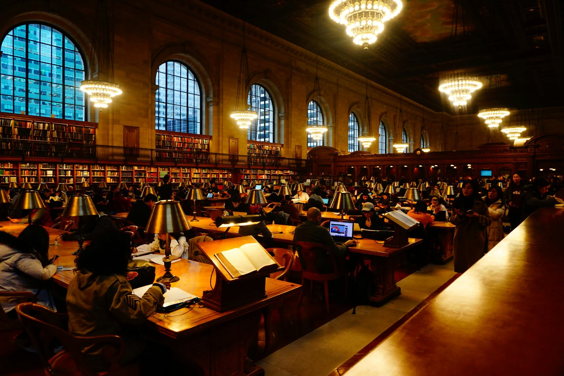 Library full of students, seated and busy on the long wooden tables