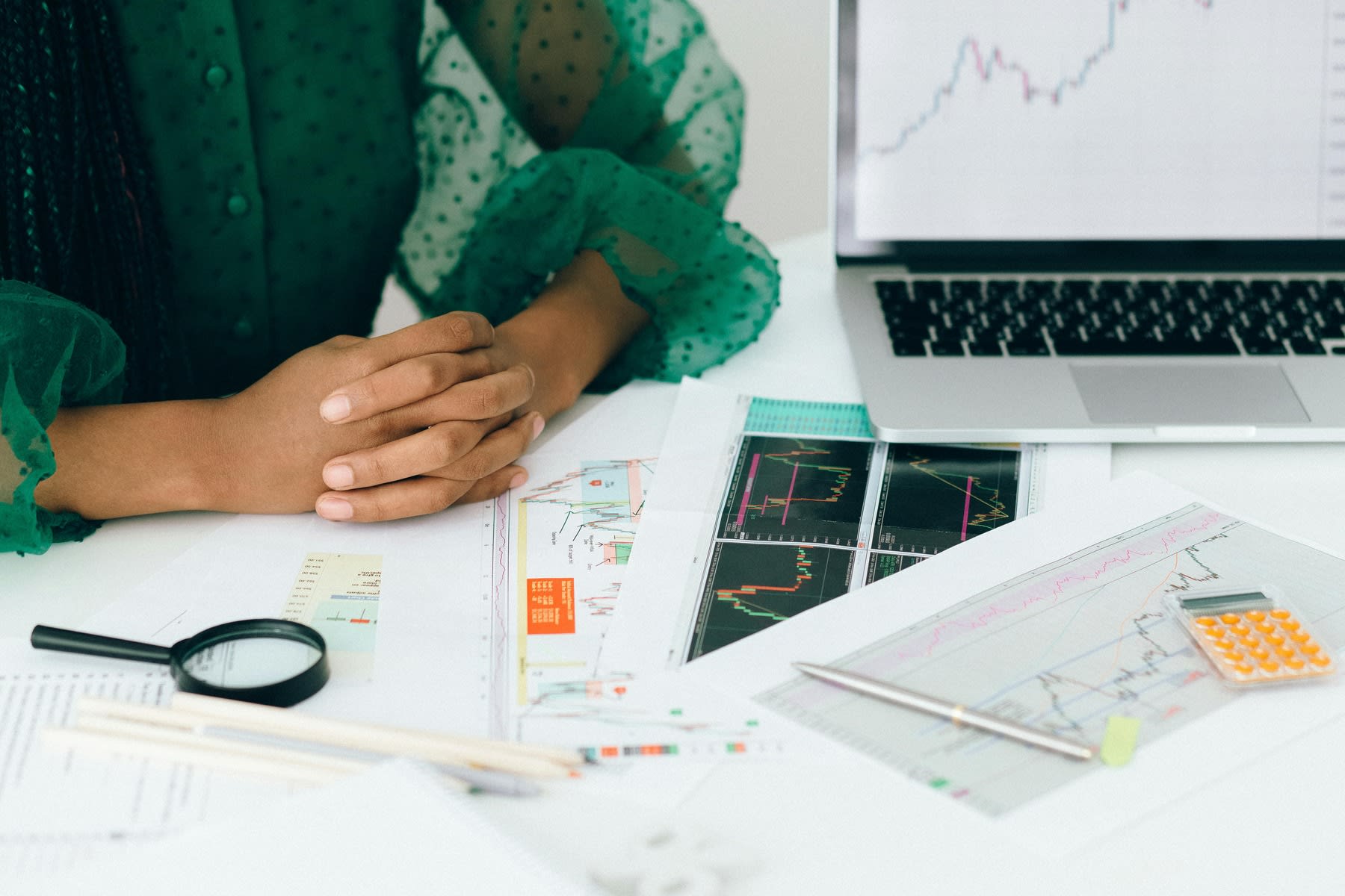 Woman sitting on a table, while her table is filled with data reports, graphs, magnifying glass and a laptop