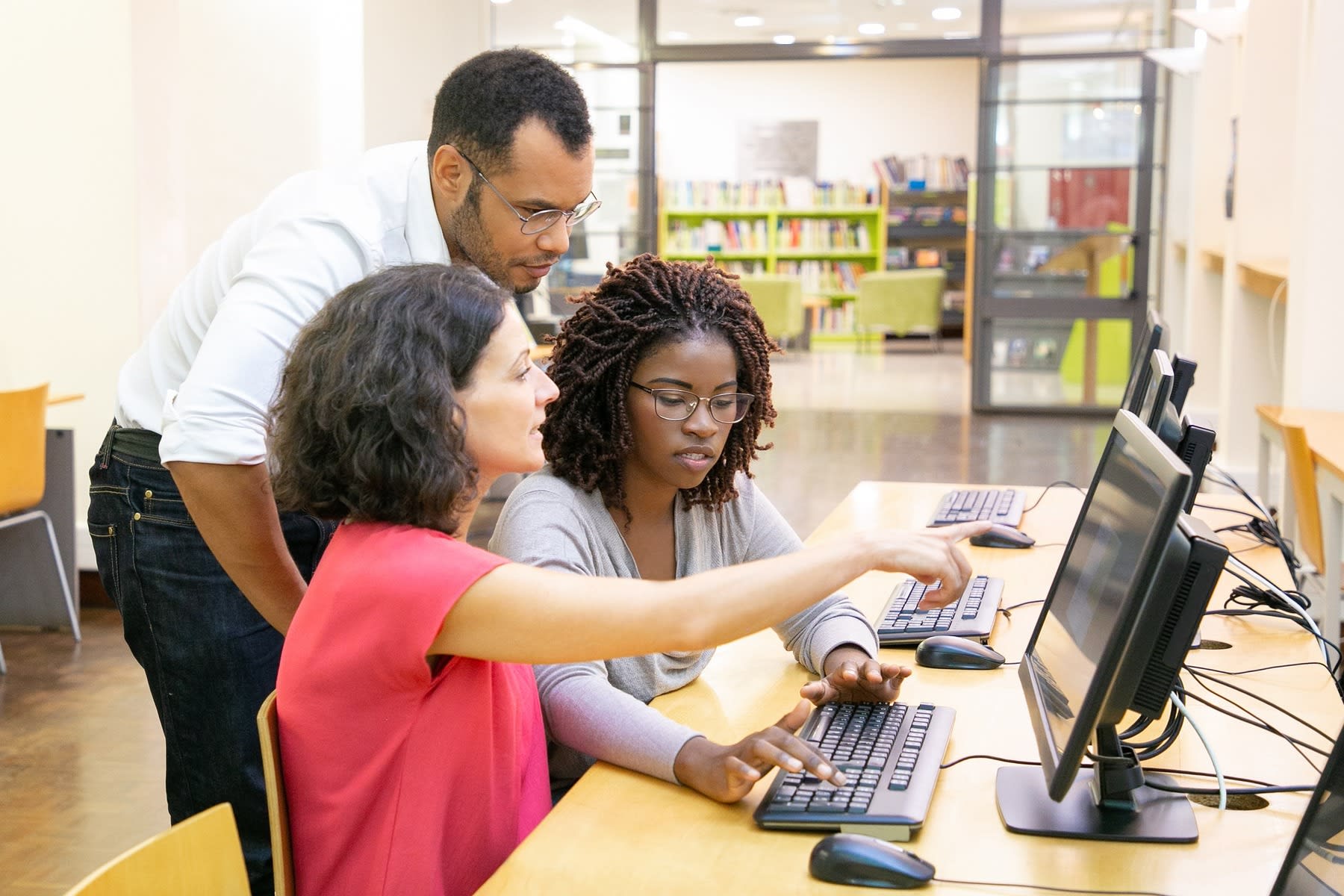 Students using one desktop on a school library while working together for their homework