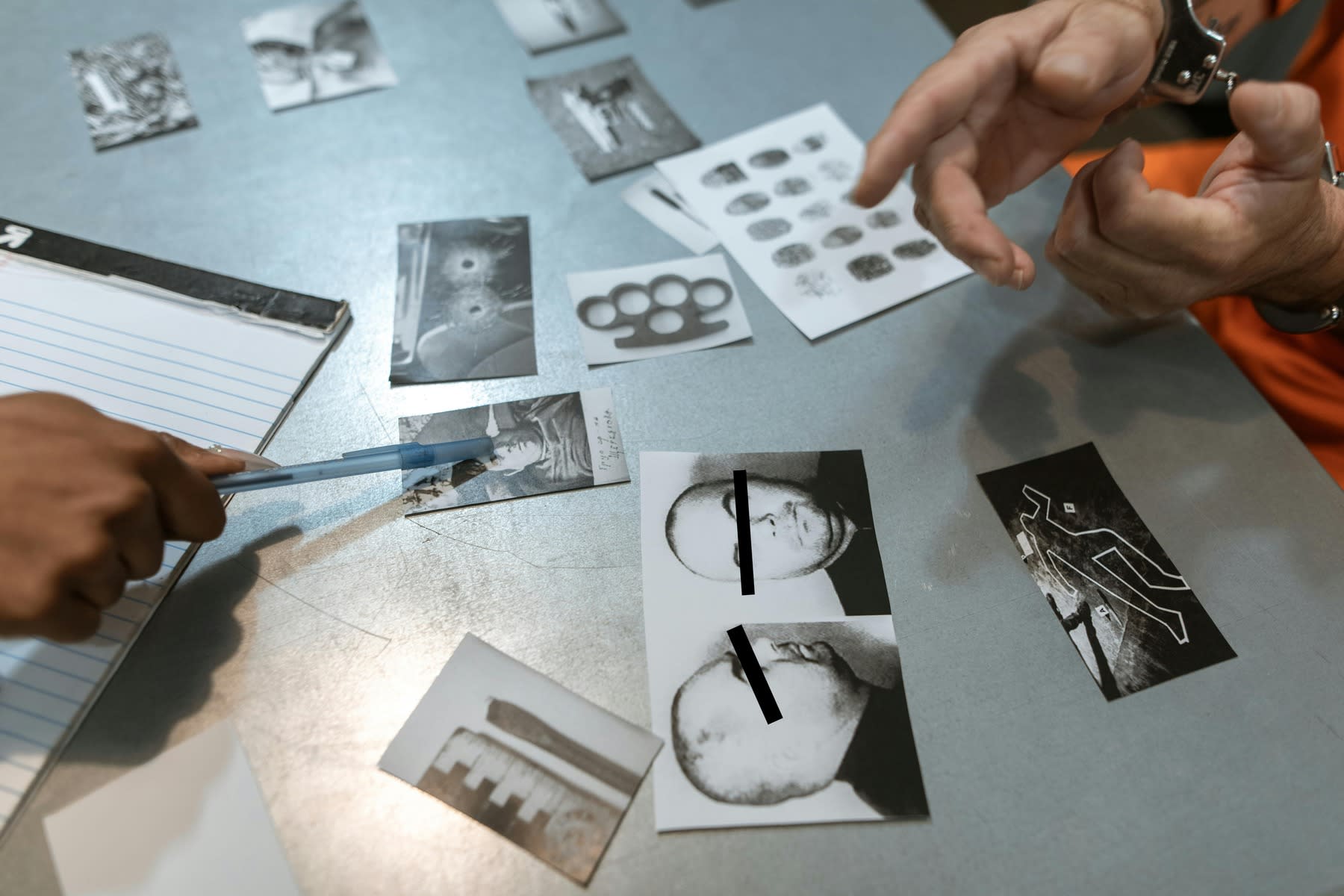 Criminologist pointing to photographic evidence while cross examining a suspect held in hand cuffs