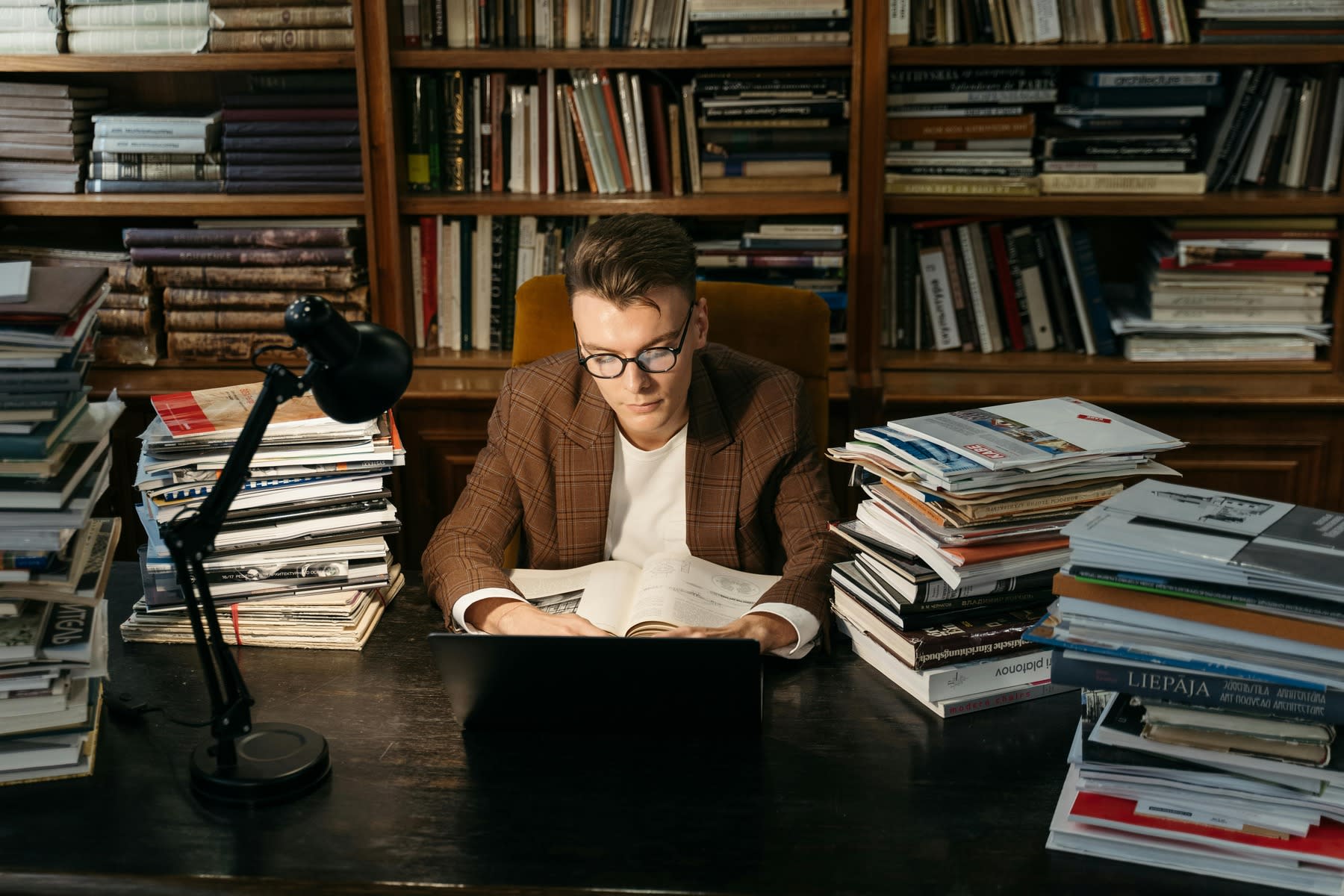 Man reading a book, while being surrounded by table full of books