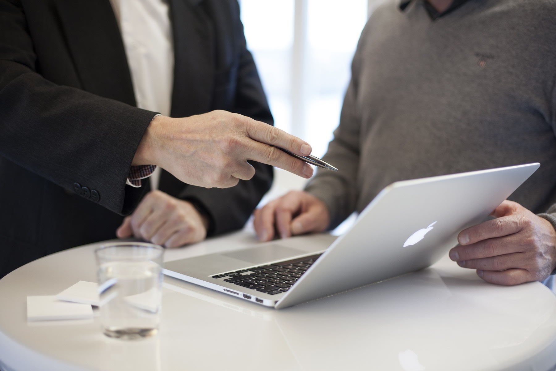 Man pointing to a laptop's monitor while talking with a colleague