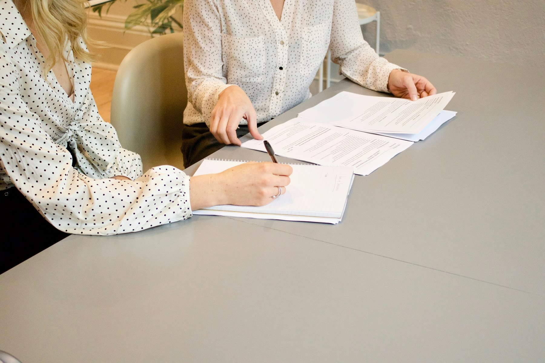 Woman signing documents, while the person seated beside her are sorting documents