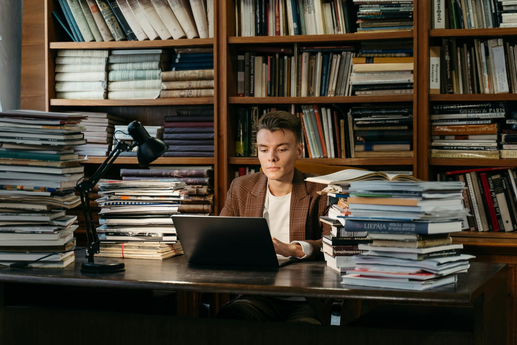 Man working on his laptop while being surrounded by a pile of books on his desk