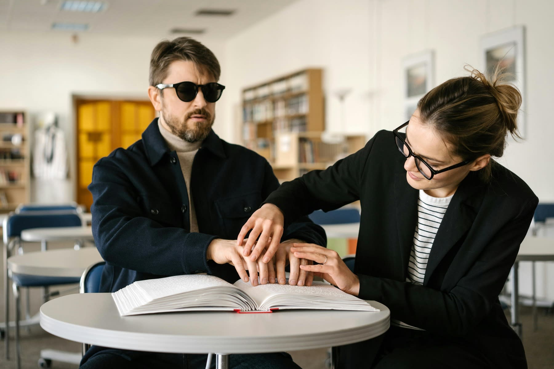 Woman guiding a blind man with his braille textbook