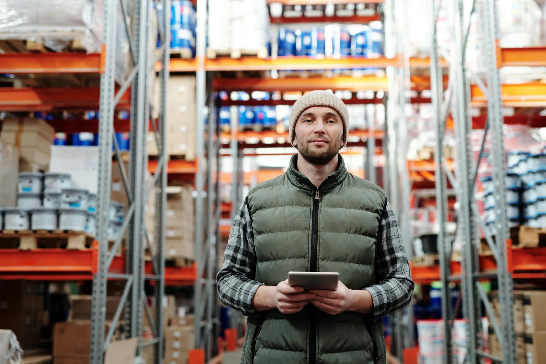 Man holding a tablet while standing in between the high shelves of a warehouse