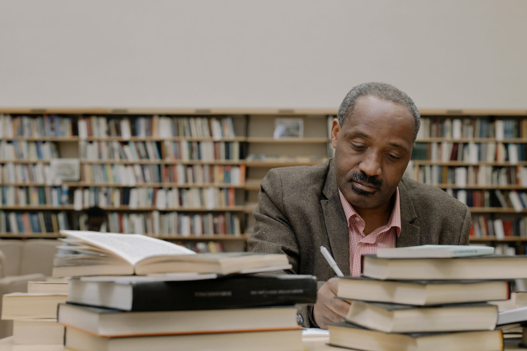 Man writing notes as his table is filled with books