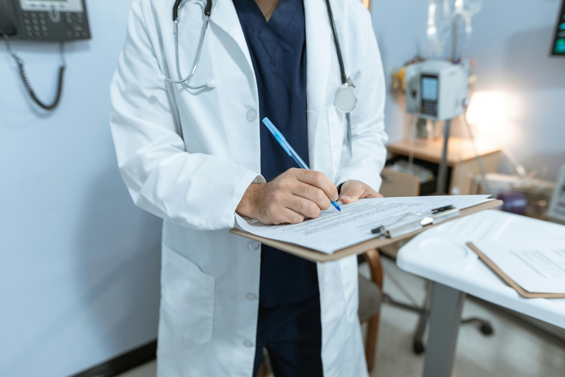 Person wearing medical coat, writing down notes on a clipboard