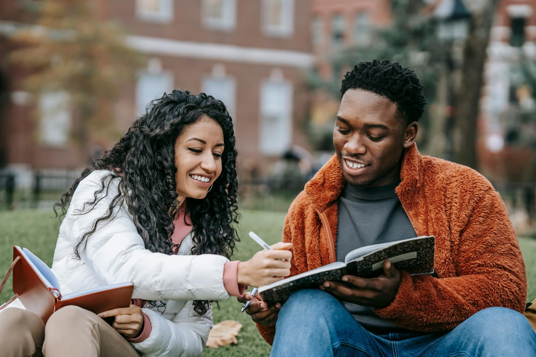 Two young people sitting on campus grounds as they both work on their homework