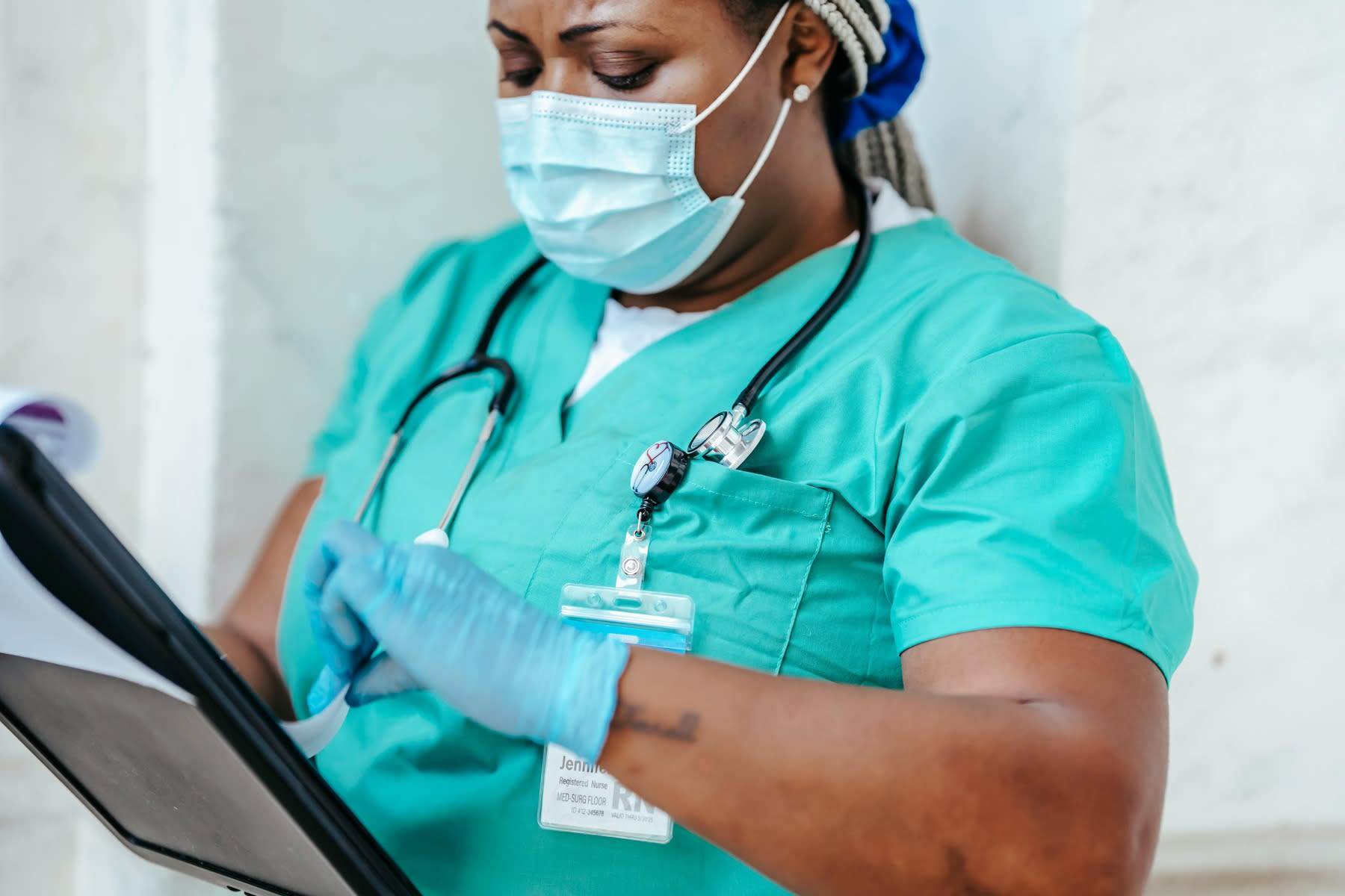 Nurse with mask and gloved hands, concentrating on reading her clipboard