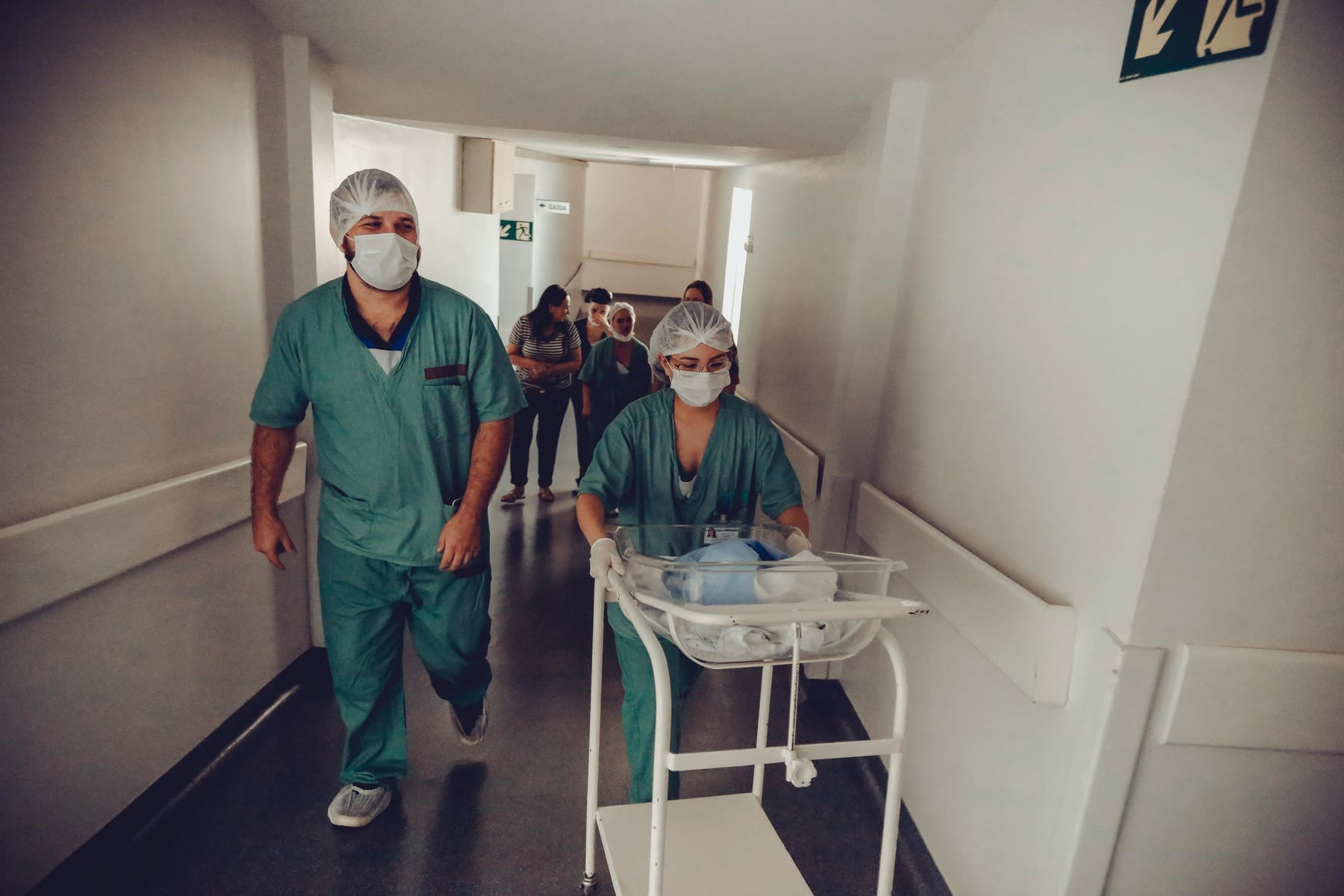 Nurse pushing a glass carriage carrying a newborn while a co-worker walks beside her