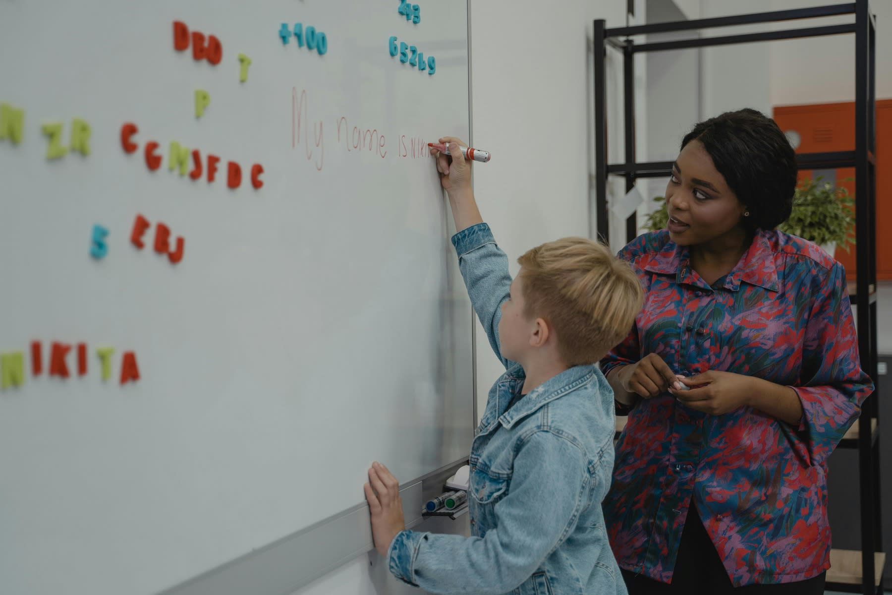 Young boy writing on a white board as a teacher looks on