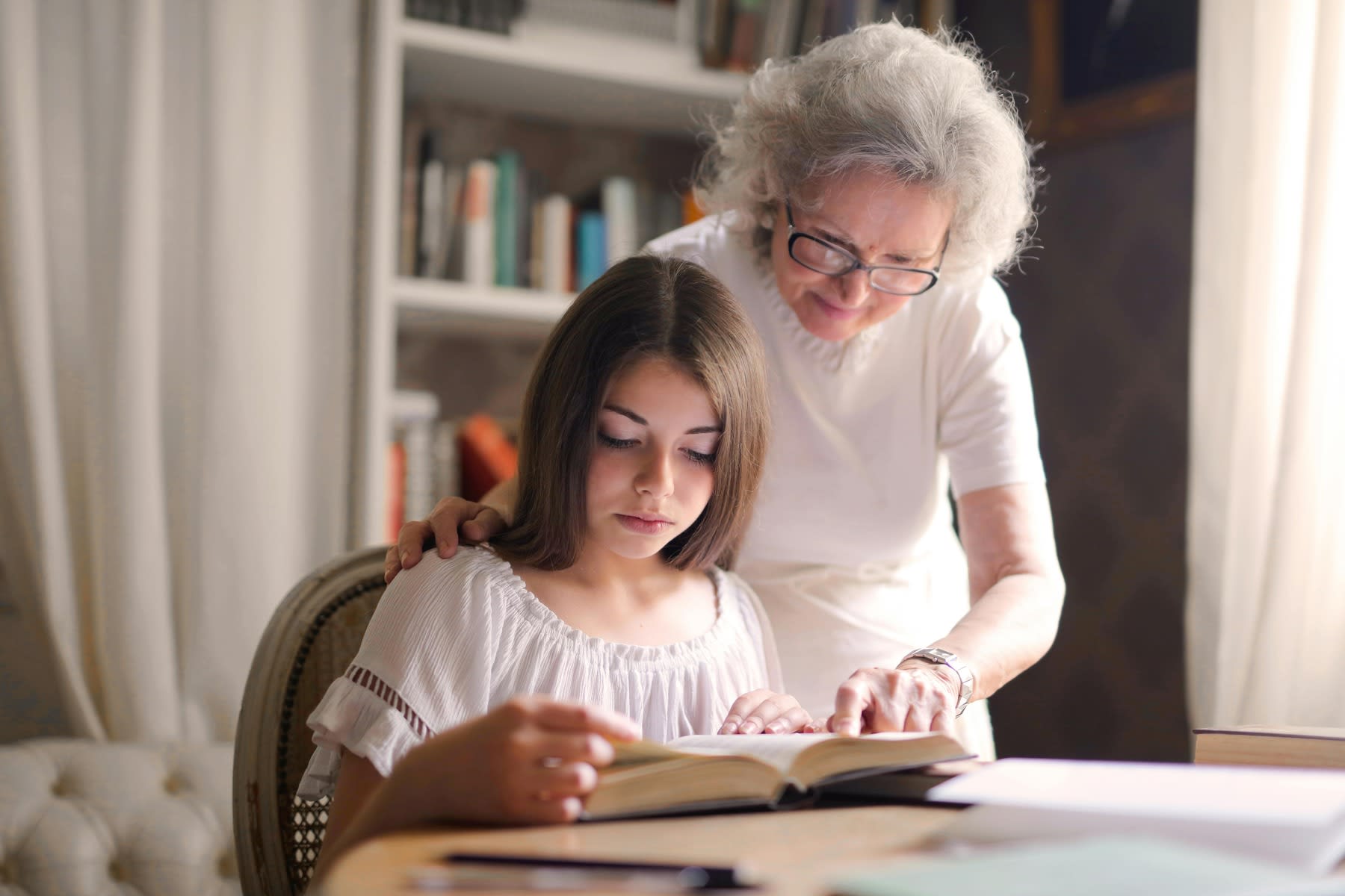 Older woman guiding a young woman as she reads