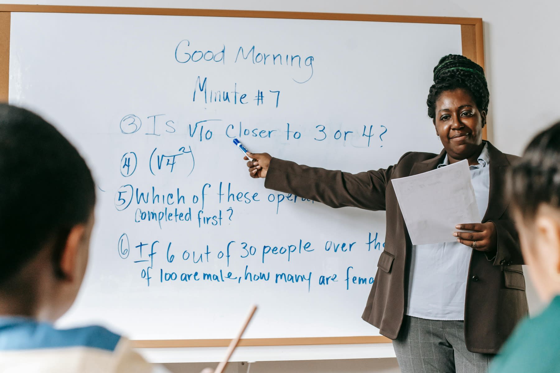 Woman pointing to the white board as she teaches a room full of students