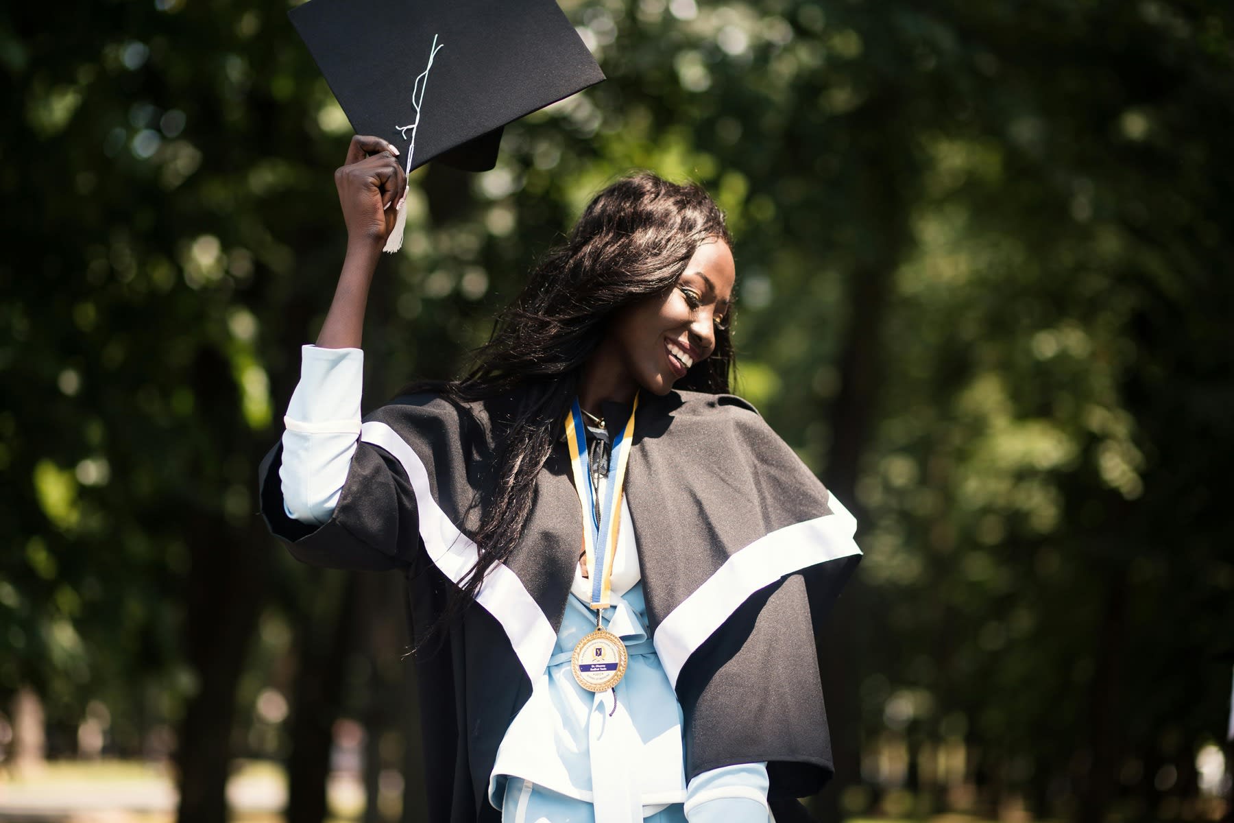 Woman wearing graduation robes while holding her graduation cap