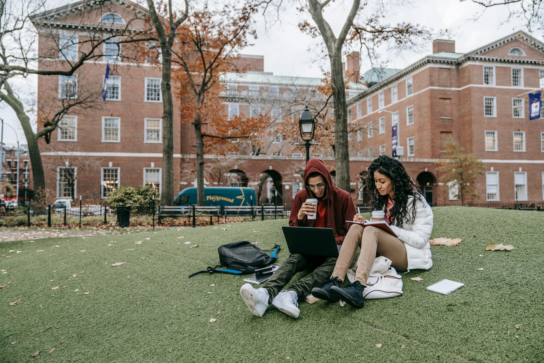 Two students sitting on the campus lawn, both studying in between classes