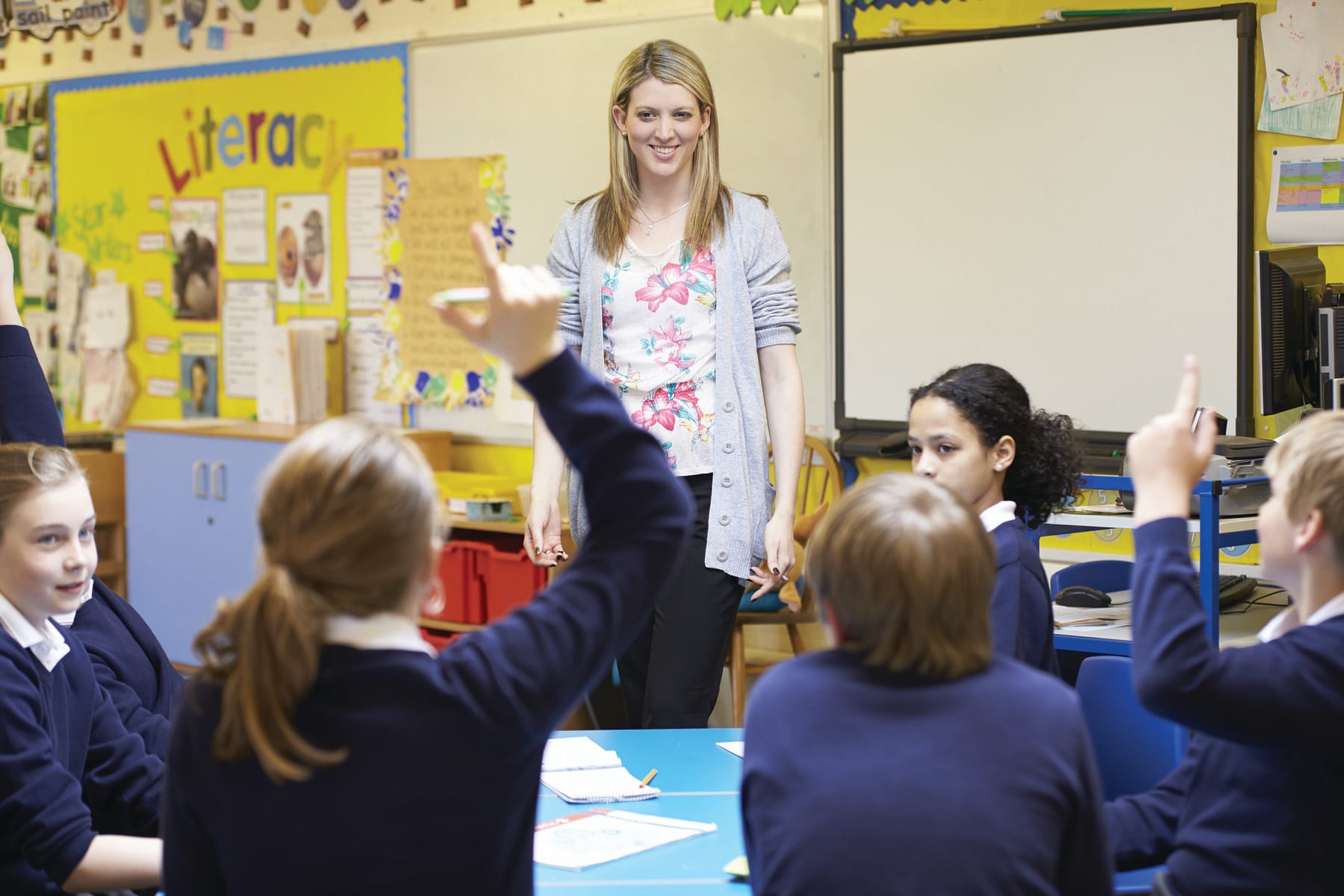 Students raising their hands while their teacher smiles in class