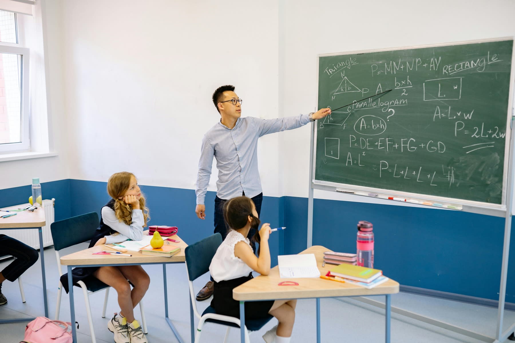 Male teacher pointing to a board while his young students are listening