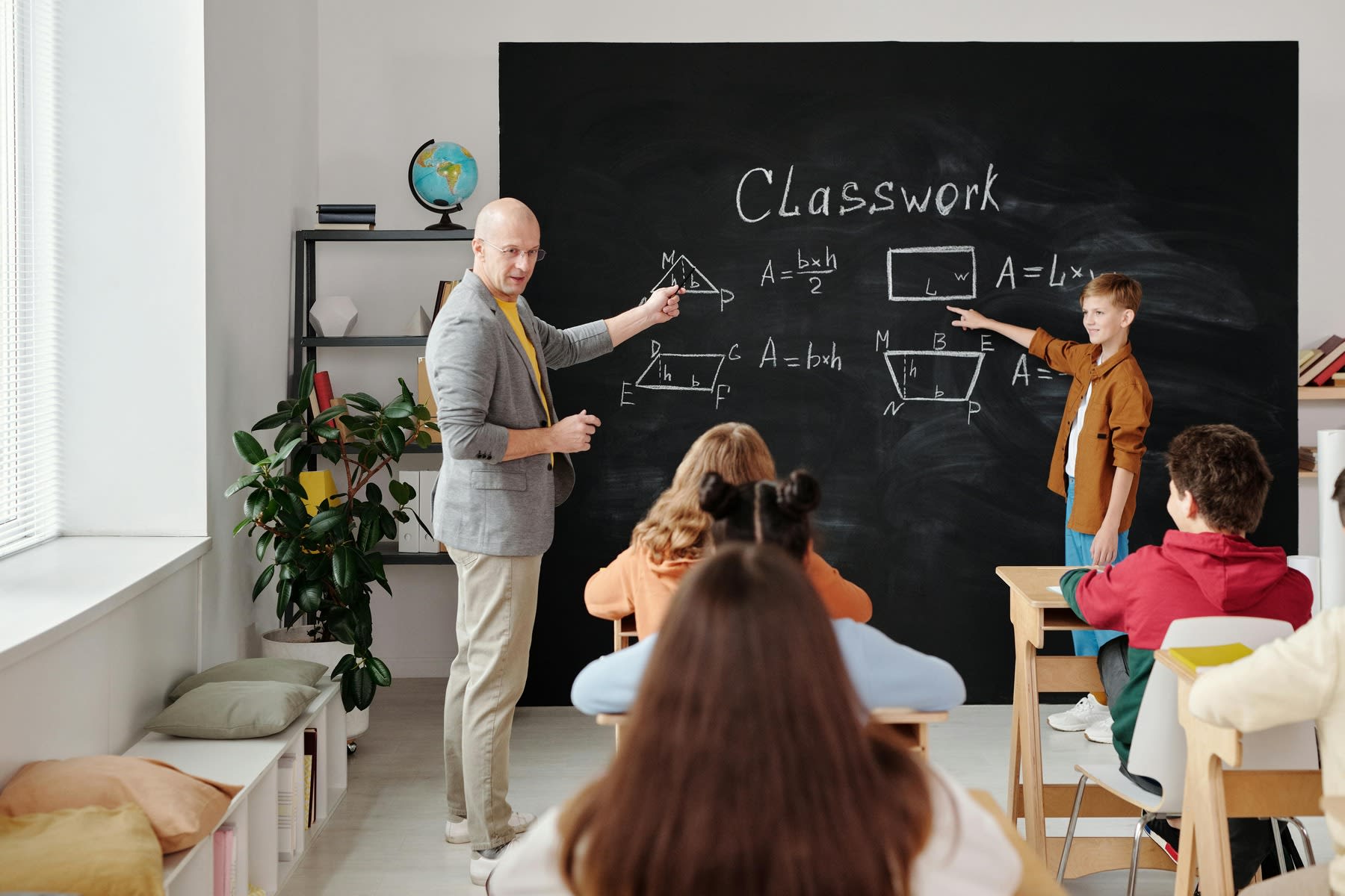 Male teacher teaching a middle school class, while a student is in front of the board answering the question