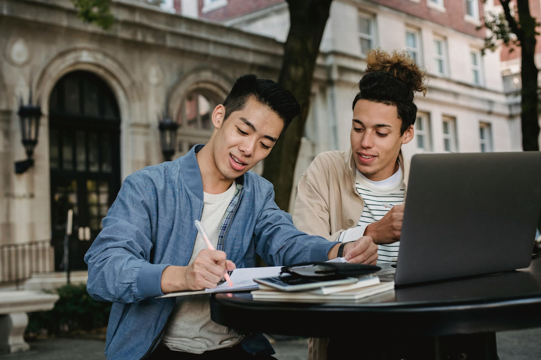 Two male students sharing notes while studying outside their campus