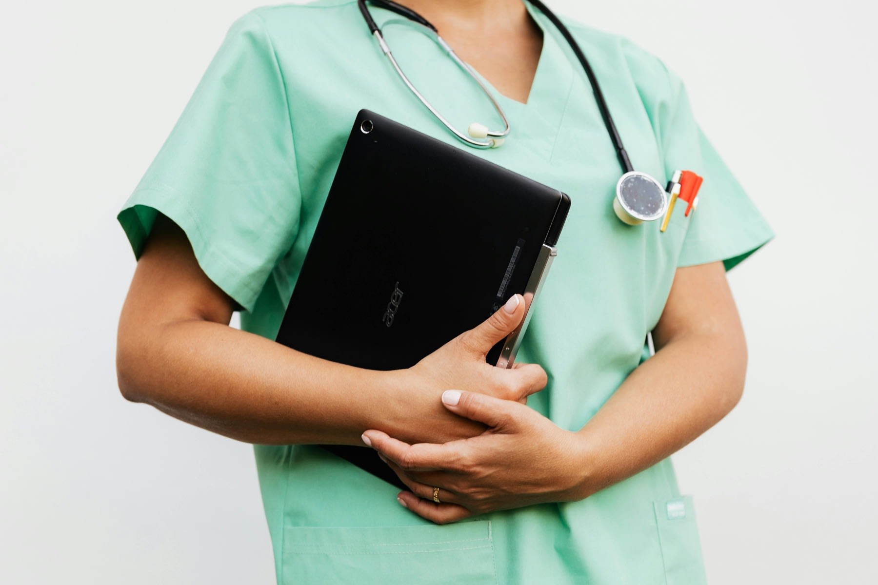 Woman wearing green nursing scrubs with a stethoscope around her neck while holding a laptop