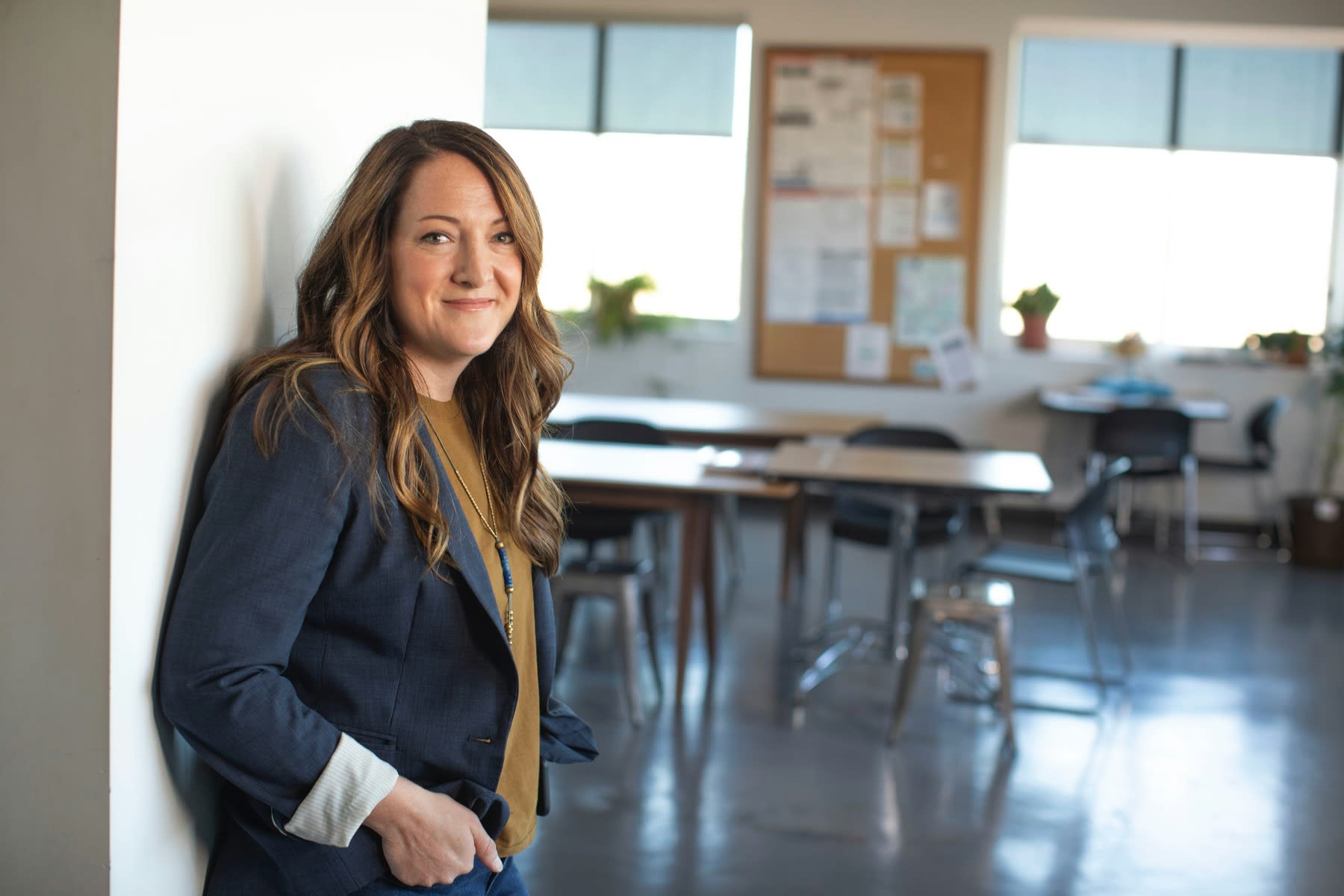Woman wearing a blazer, smiling while standing outside a classroom
