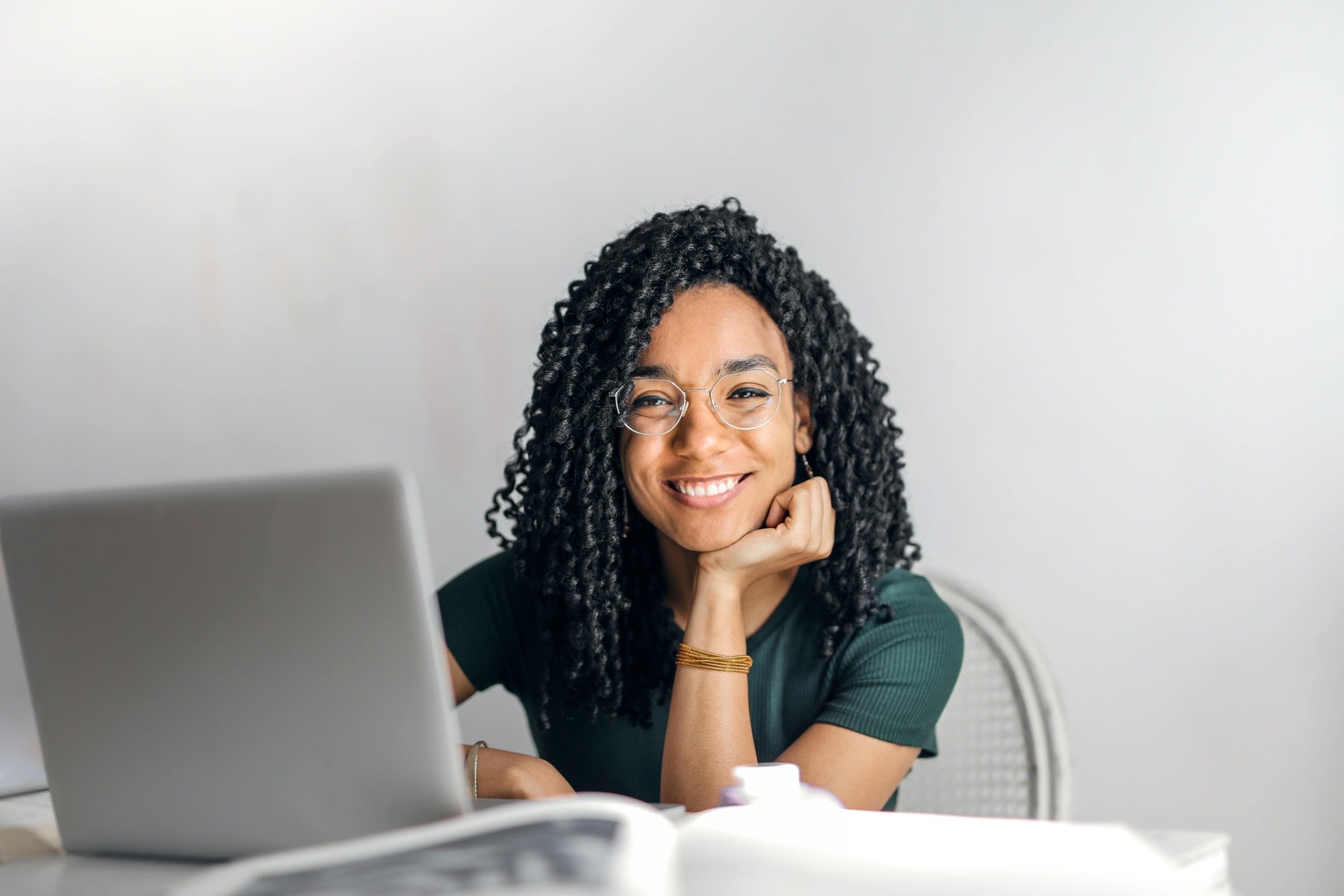 Woman resting her chin on her palm, while smiling and in front of her laptop