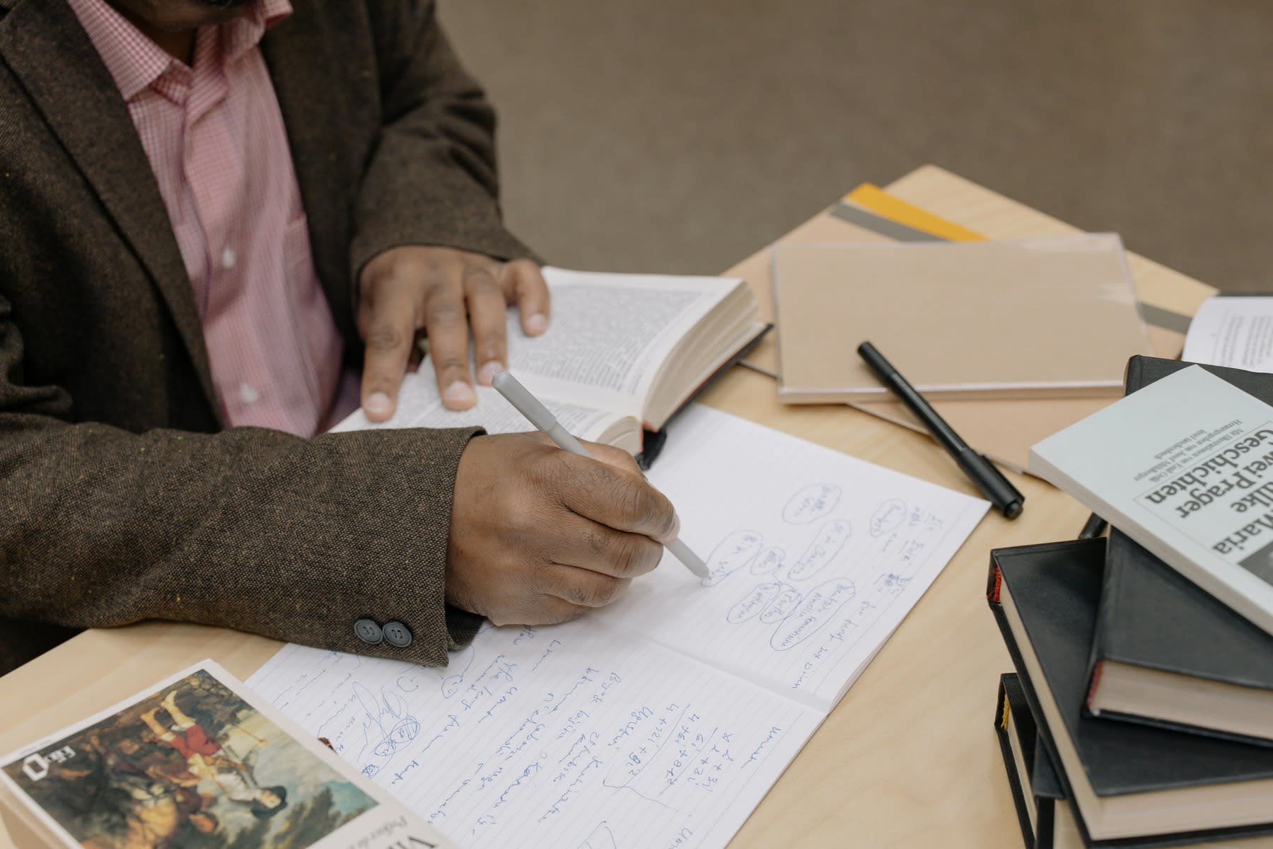 Man writing down notes as he reads from his pile of books on the table