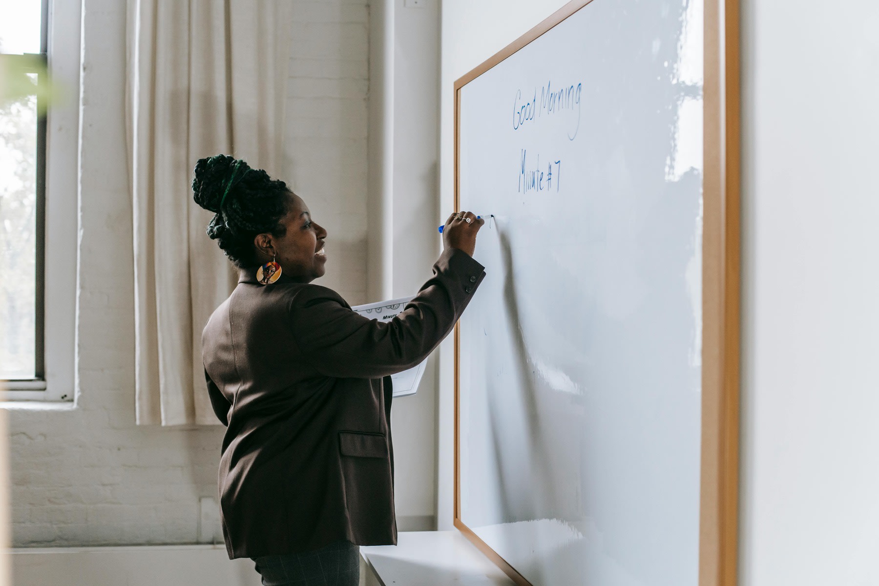 Woman writing on a white board while holding a class