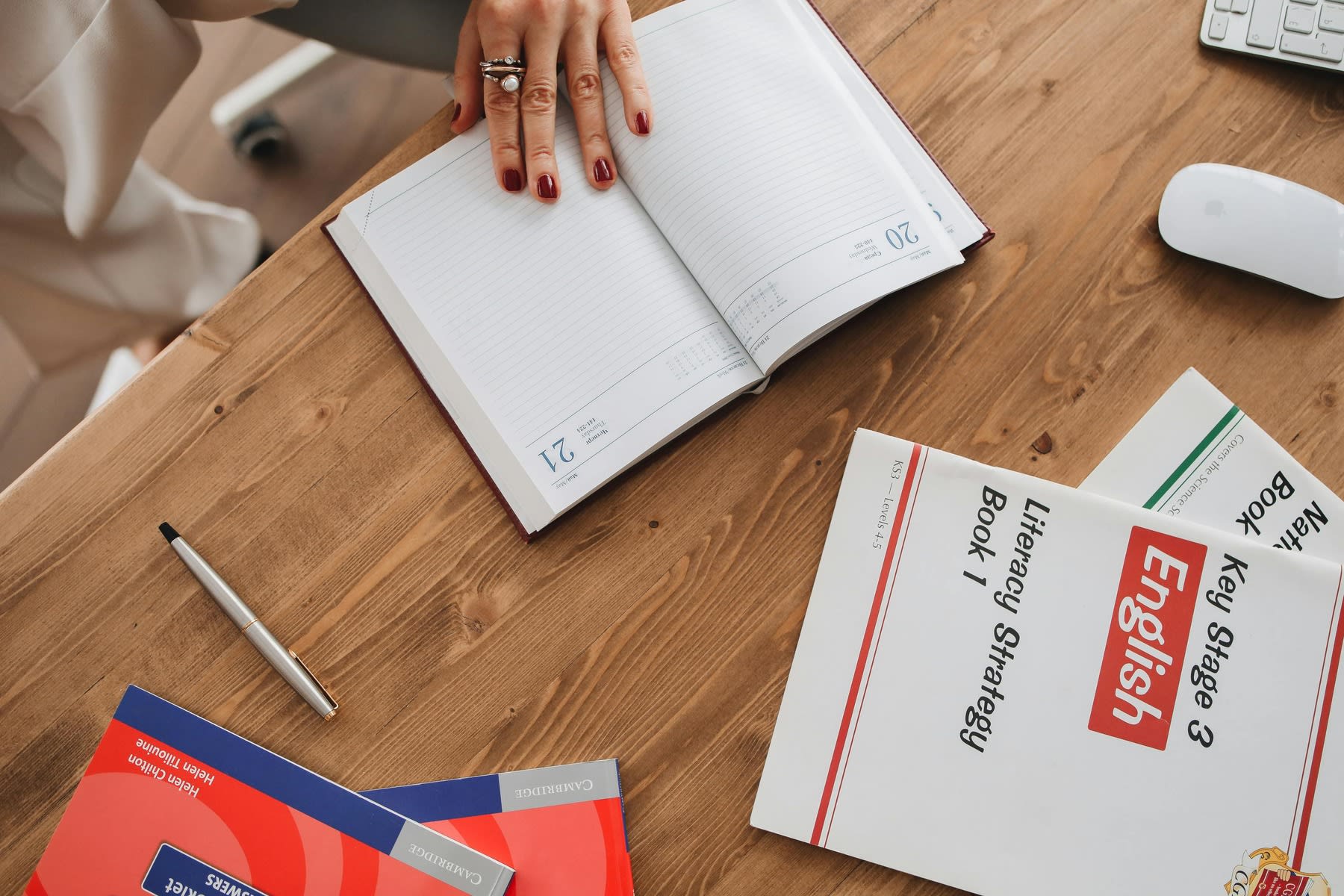 Woman opening to a blank page of a notebook, while her English workbook and other materials are on the same table