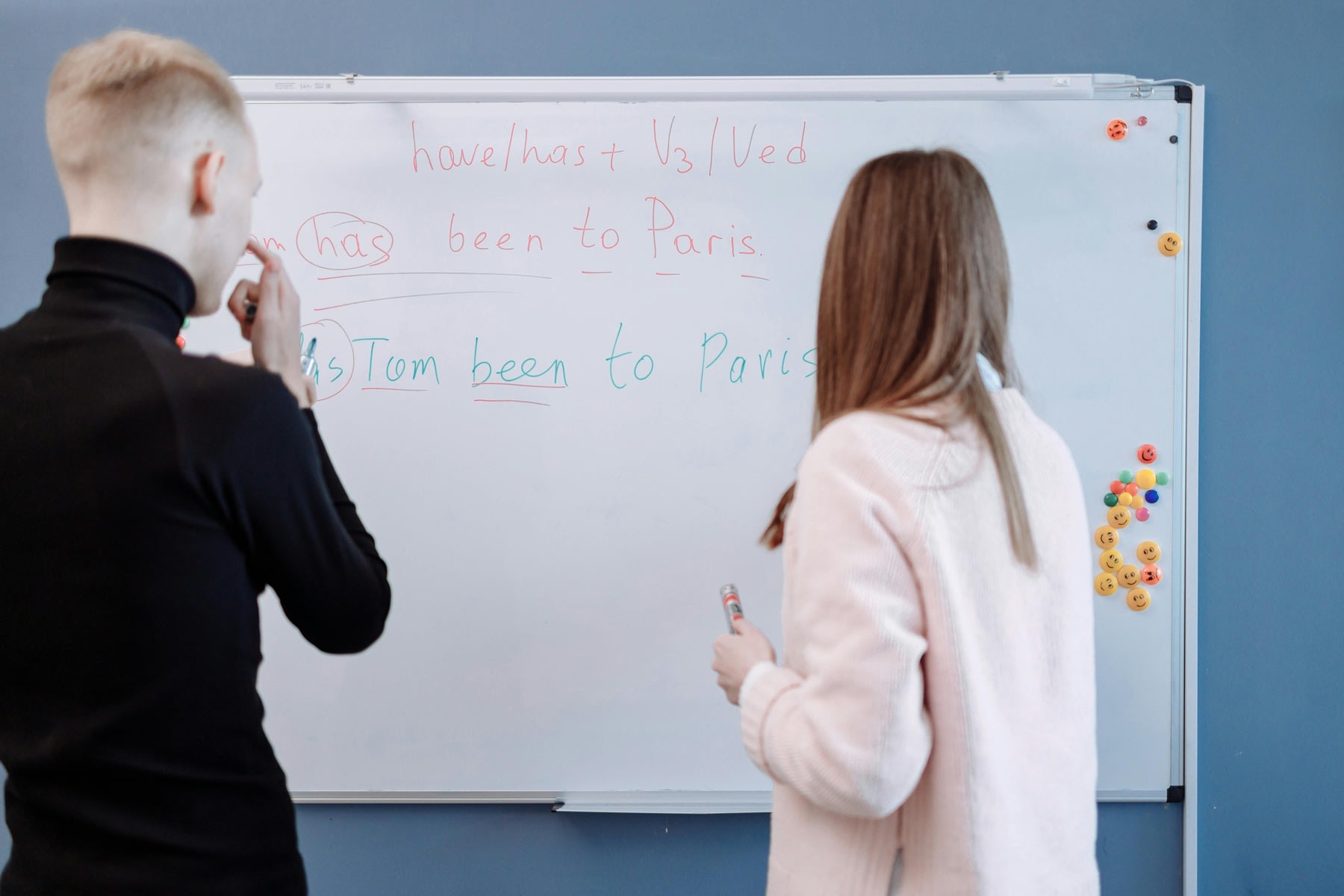 Woman writing her English lessons on a white board while a young male student is observing