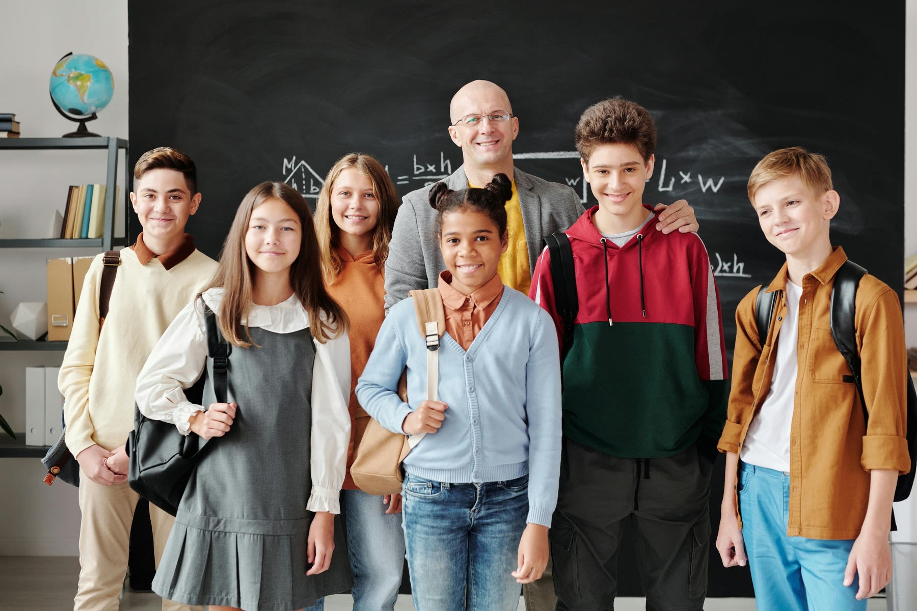 Male teacher posing for a photo with his elementary students in front of his classroom