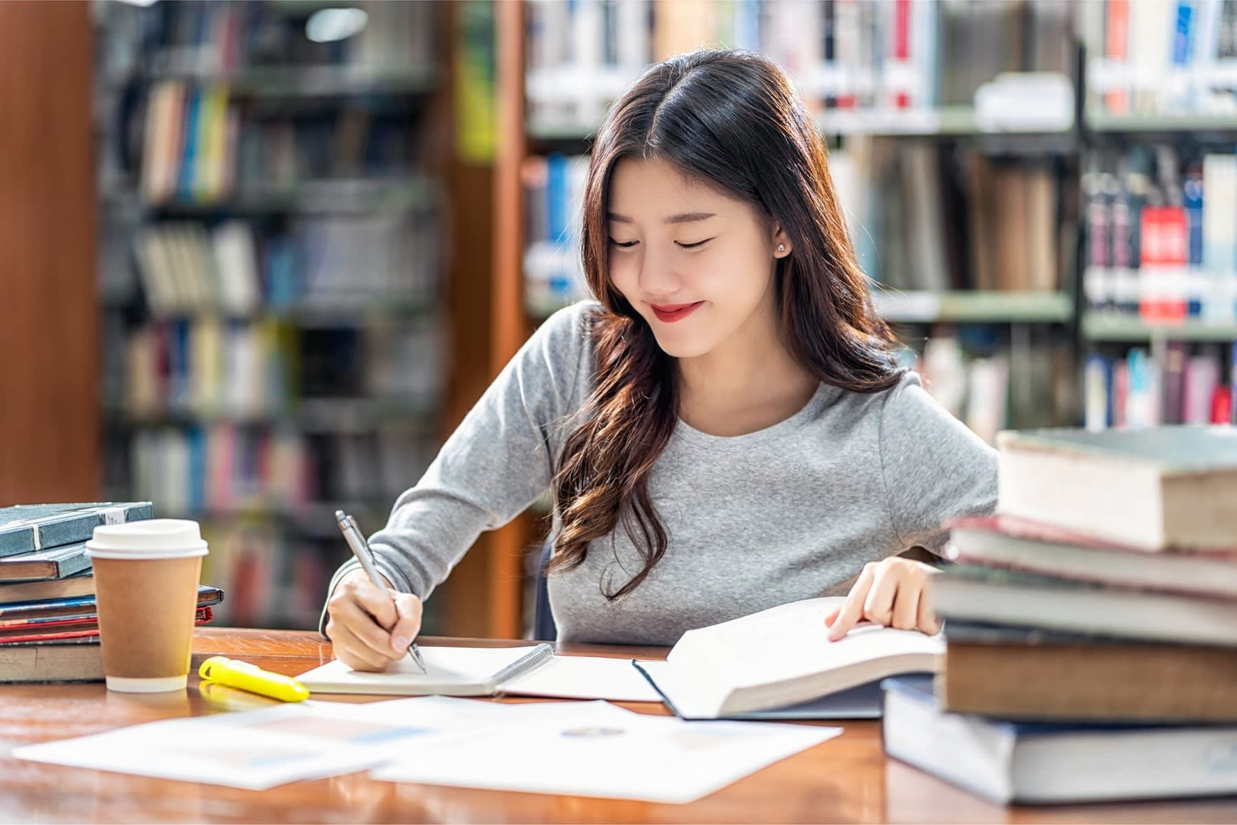 Woman writing notes as she reads from the pile of books on her table