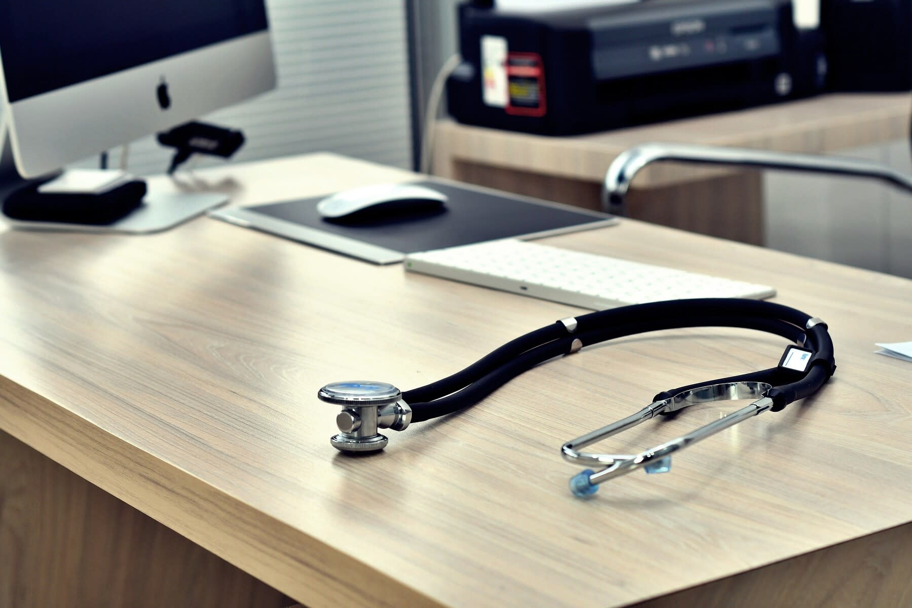 Stethoscope on a wooden desk, right next to a desktop monitor and keyboard
