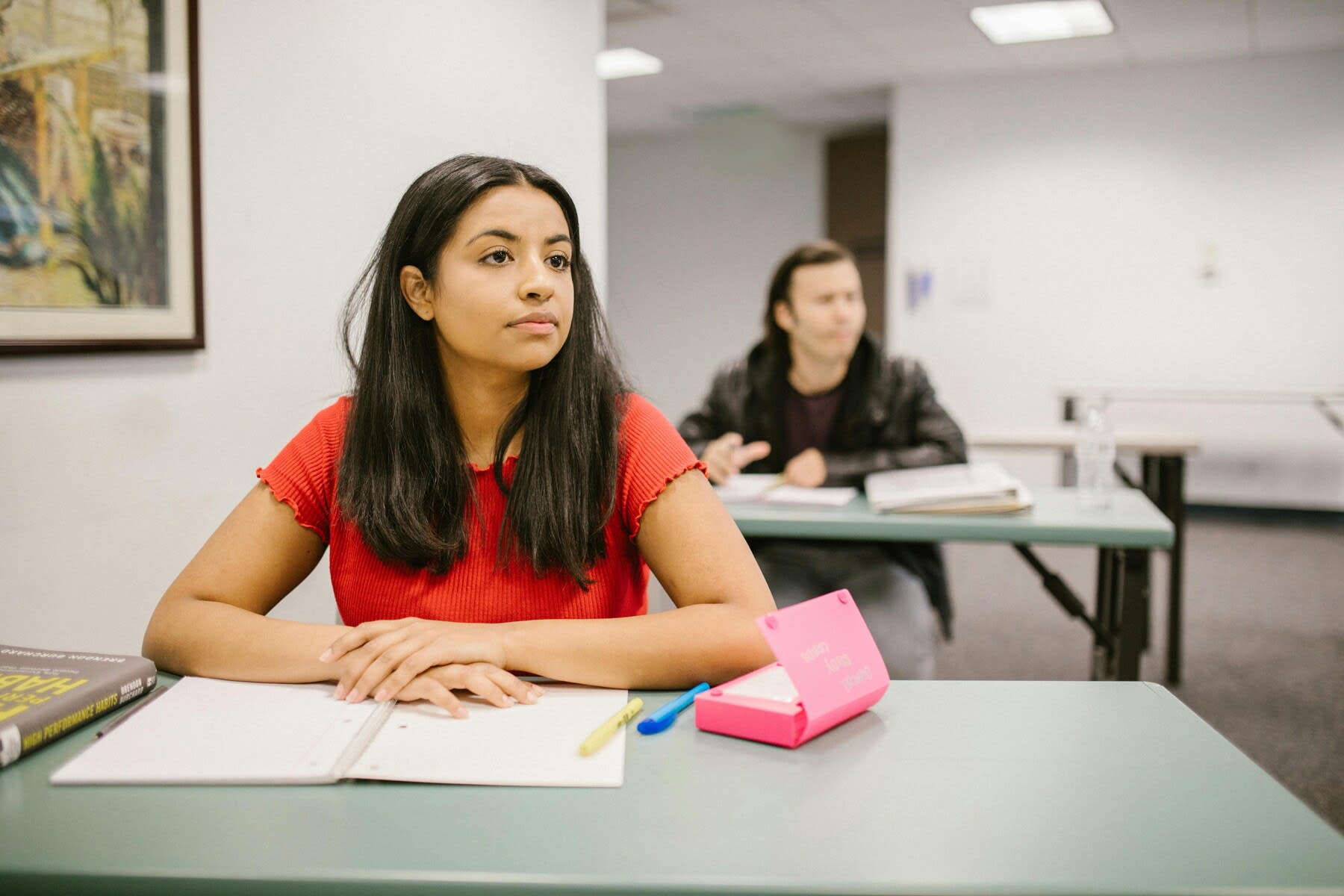 Young female student sitting in class while her notebook and pencil case are open