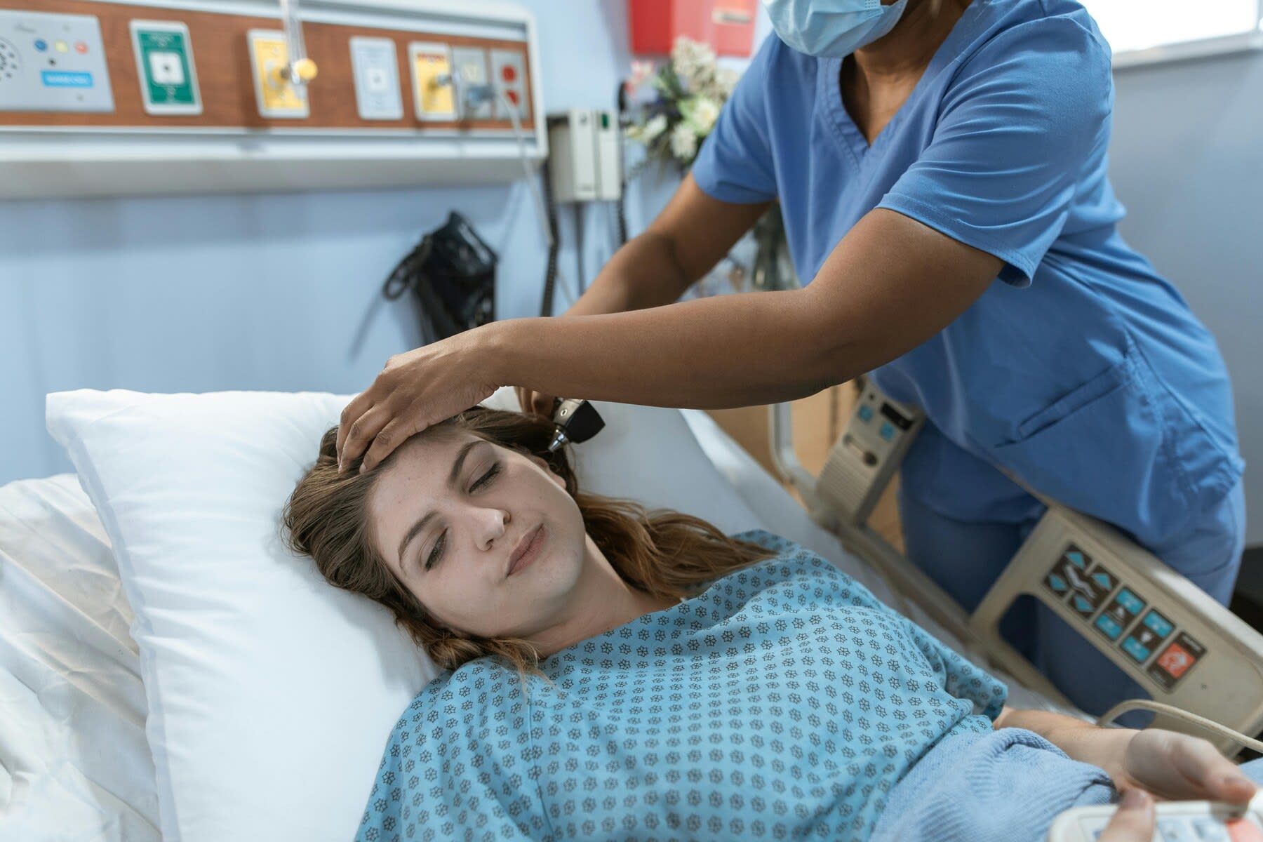 Nurse taking a female patient's temperature while she's lying on a hospital bed