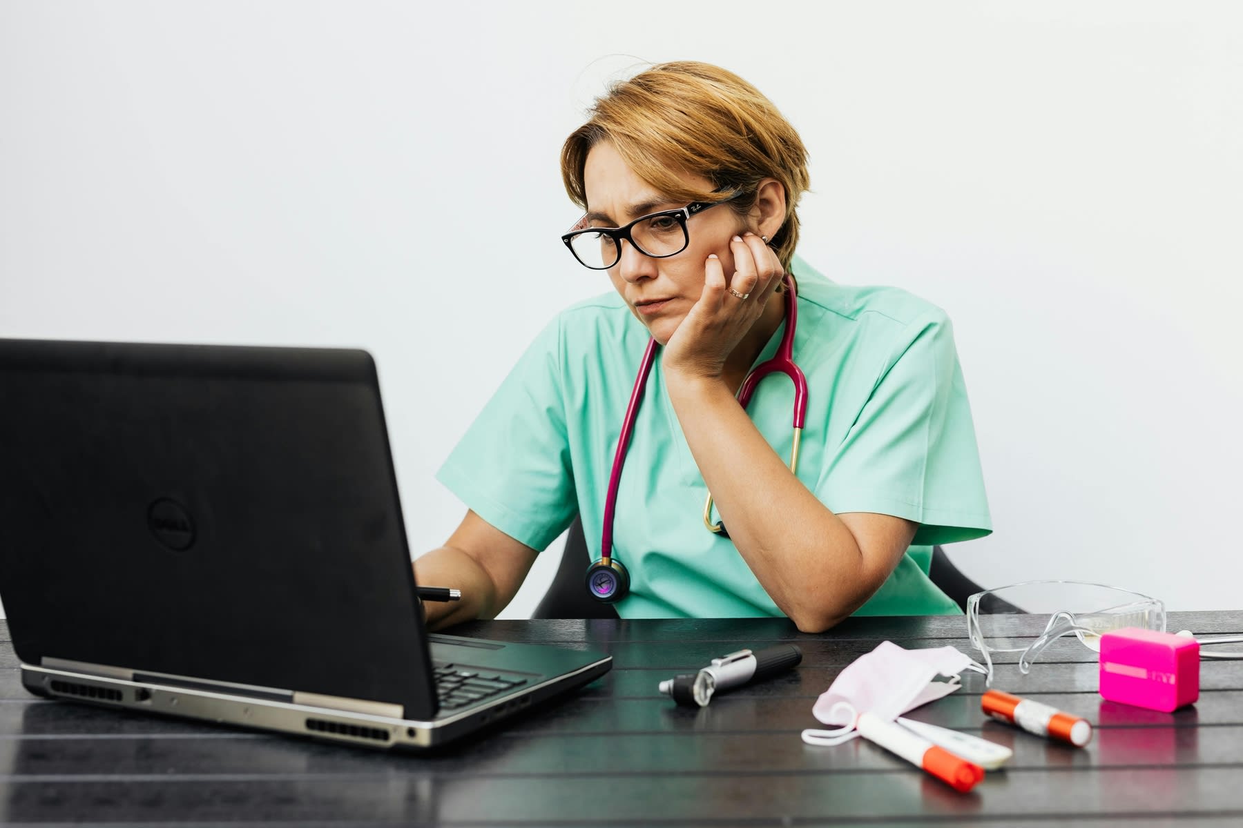 Female nurse with a stethoscope around her neck, browsing through her laptop at work