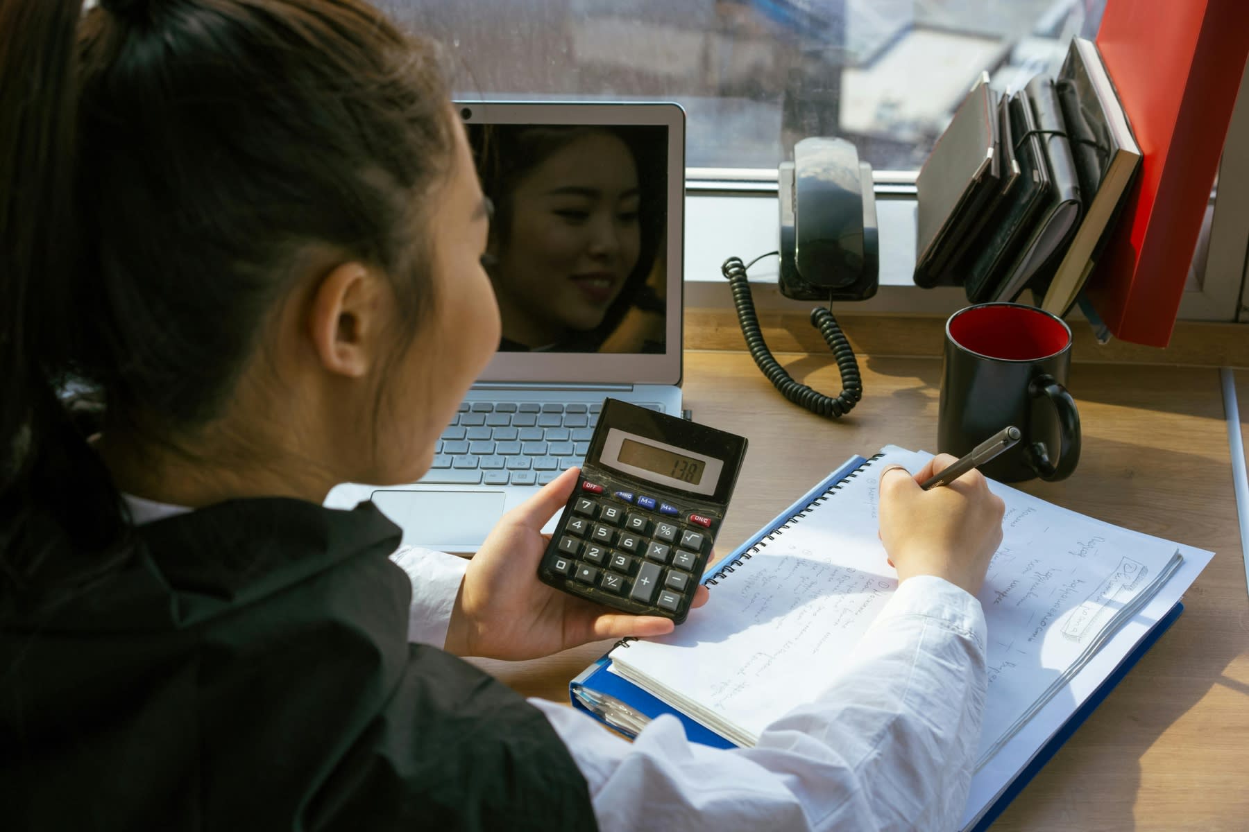 Woman holding a calculator while writing down notes