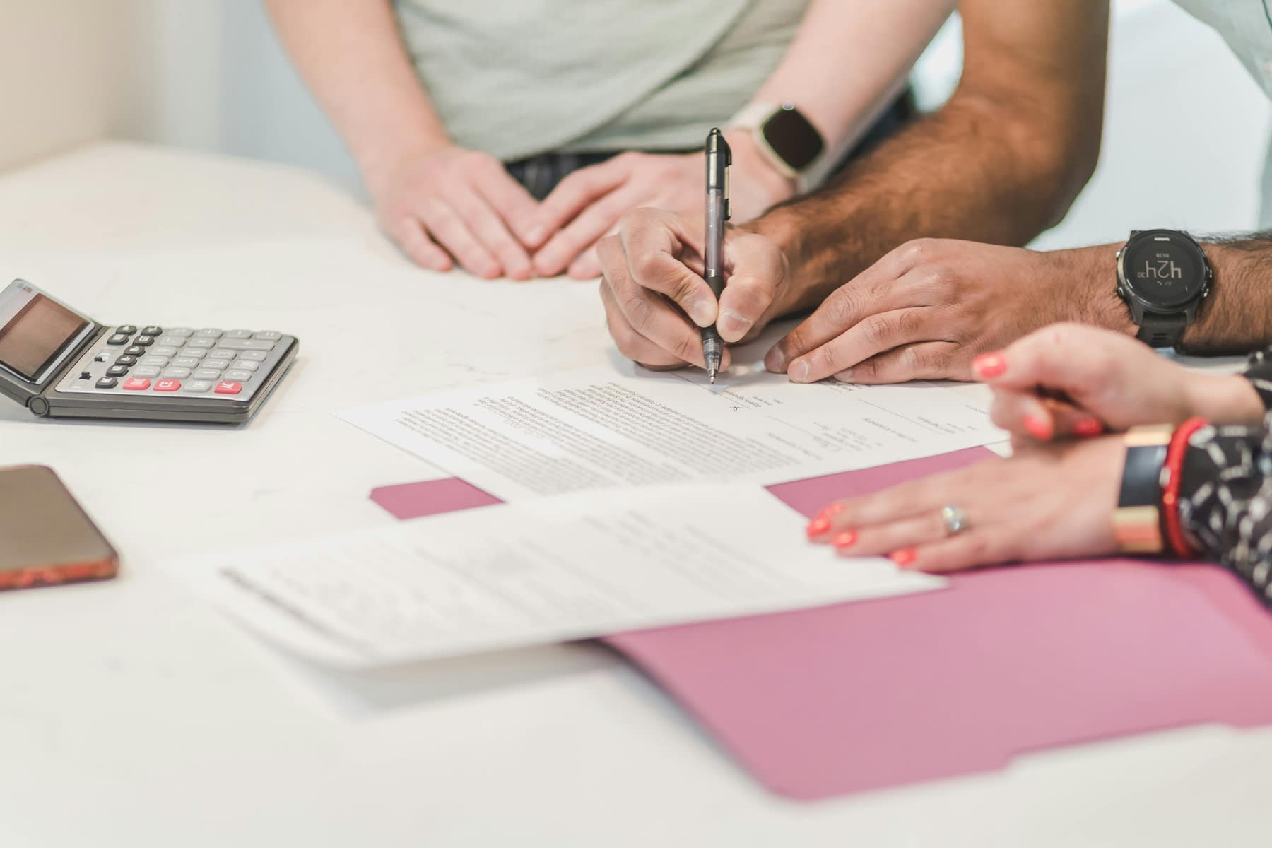 Man signing a printed document while others are seated beside him on a table