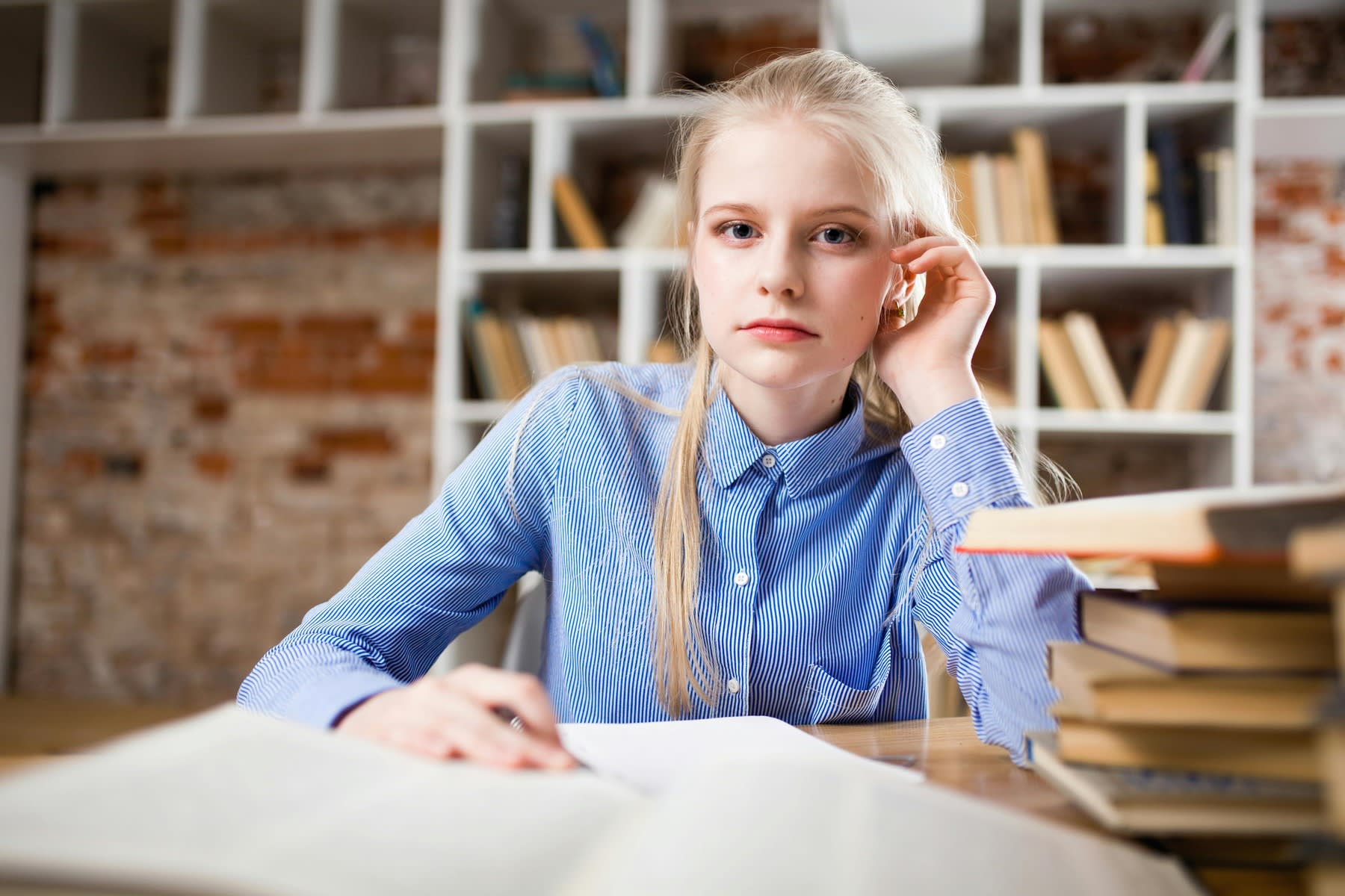 Female student looking serious while a stack of books are on her desk table