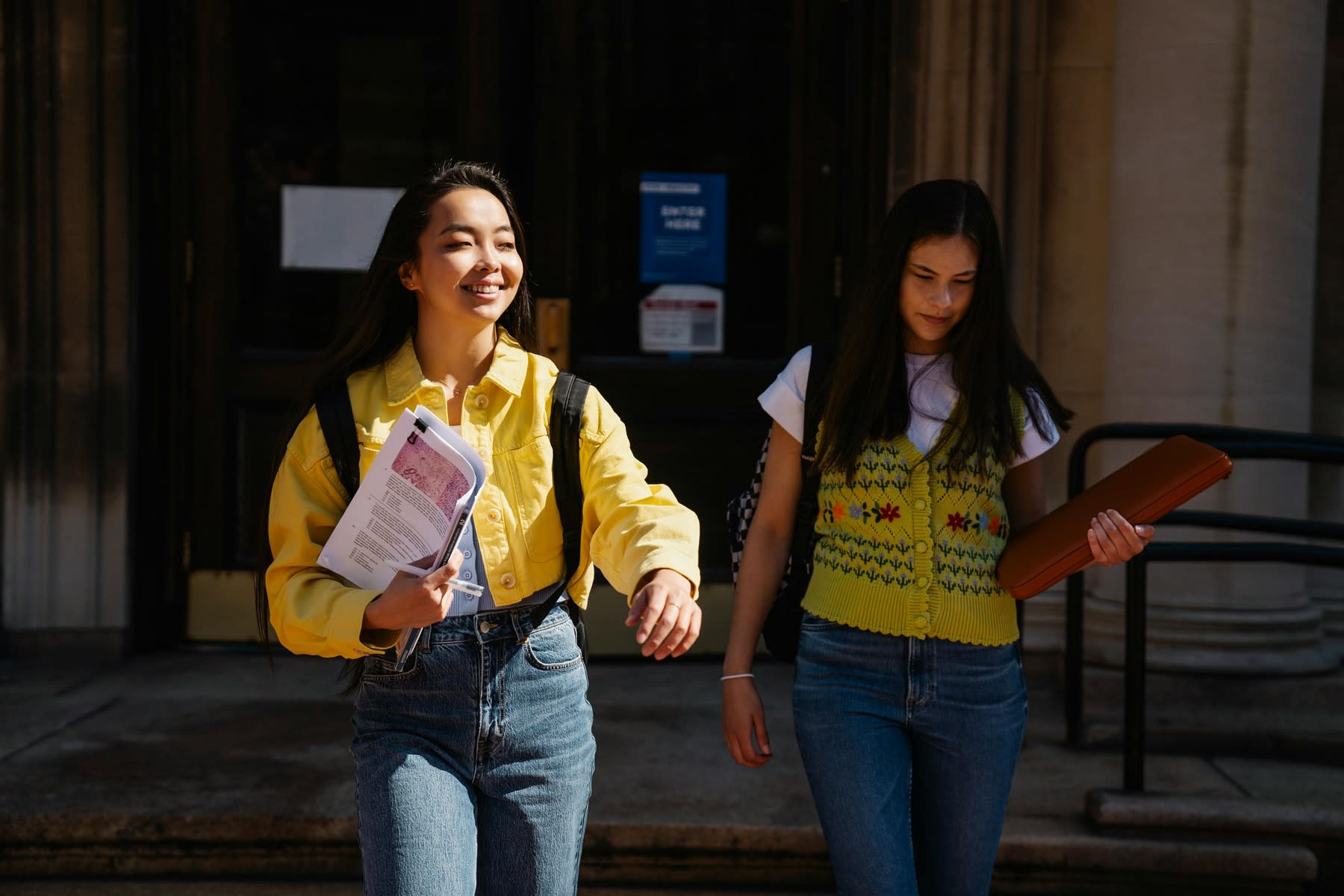 Two young female students coming out of school, holding folders and papers