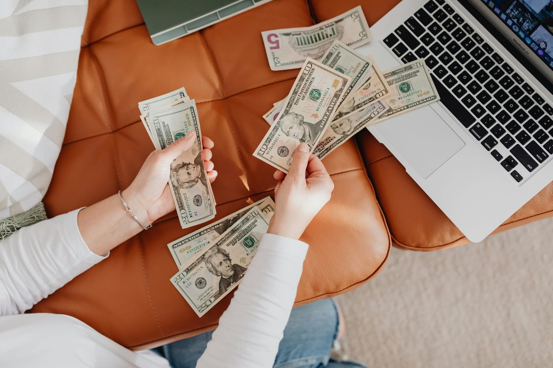 Woman counting dollar bills in front of a laptop