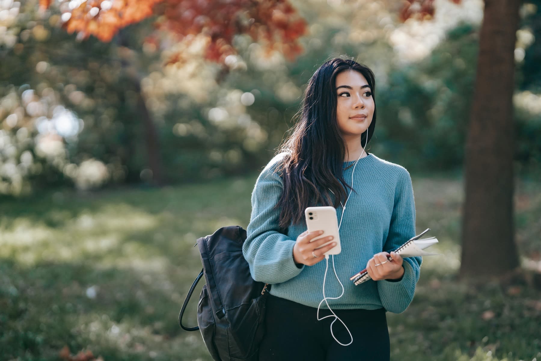 Woman holding a white smartphone while carrying her backpack and books