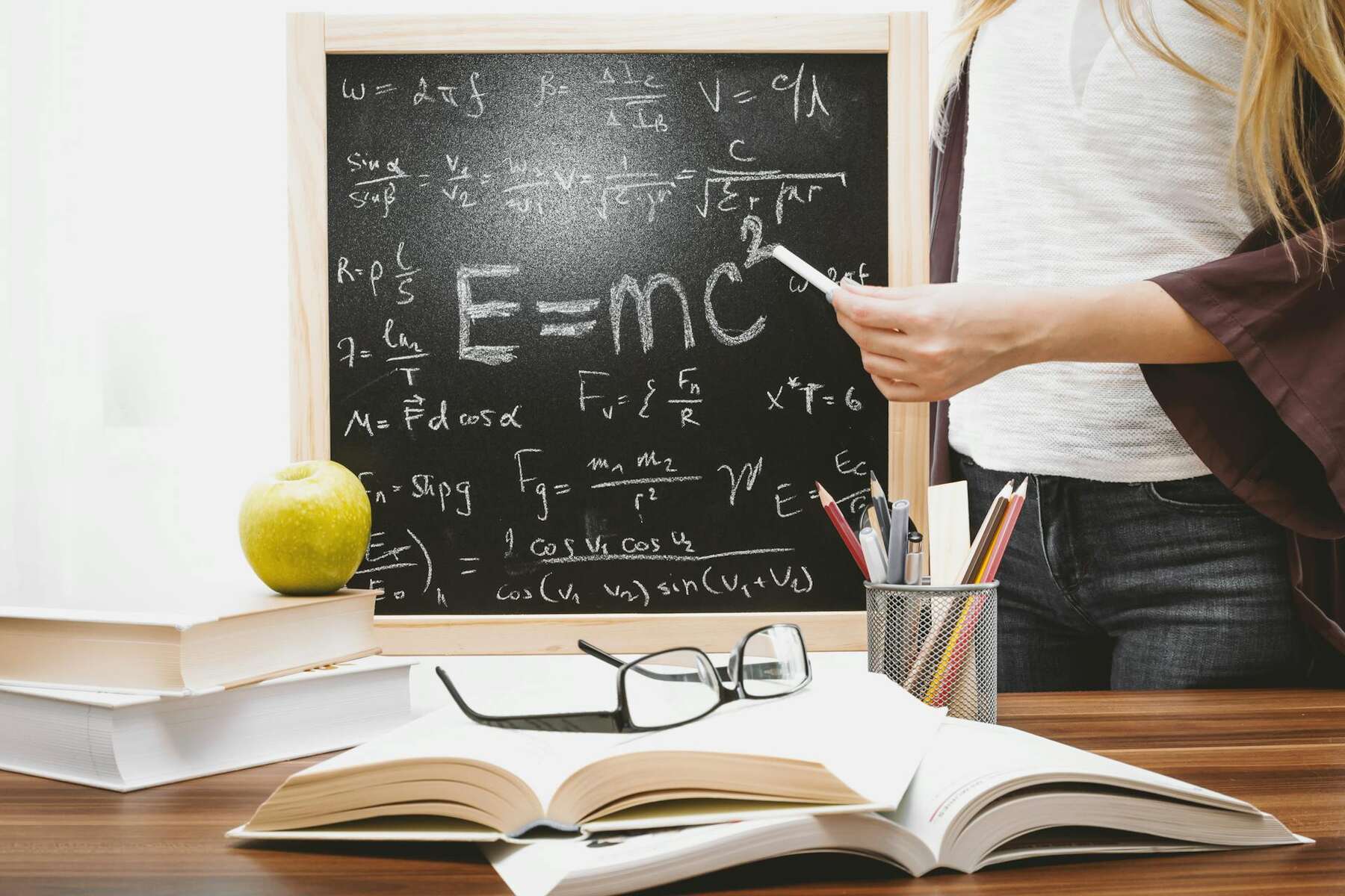 A woman writes on a blackboard with chalk, focused on her task in a classroom