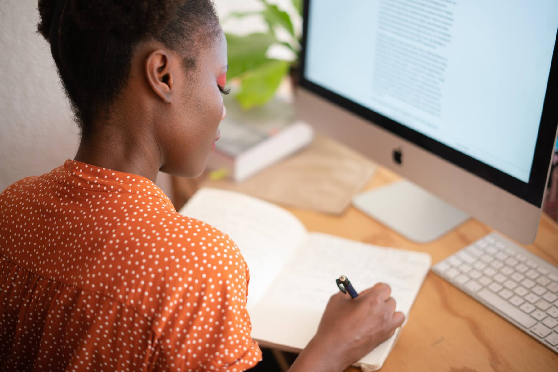 Woman writing notes on her notebook while using her desktop monitor