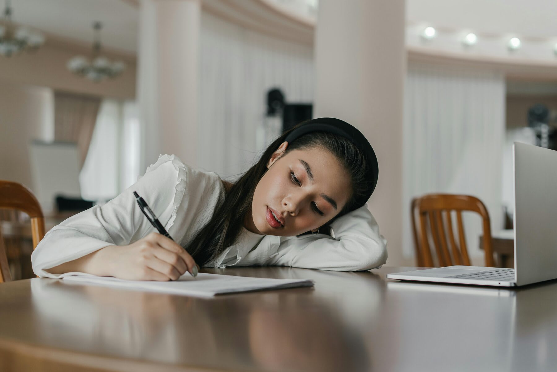 Woman writing notes while her head is slumped close to the table
