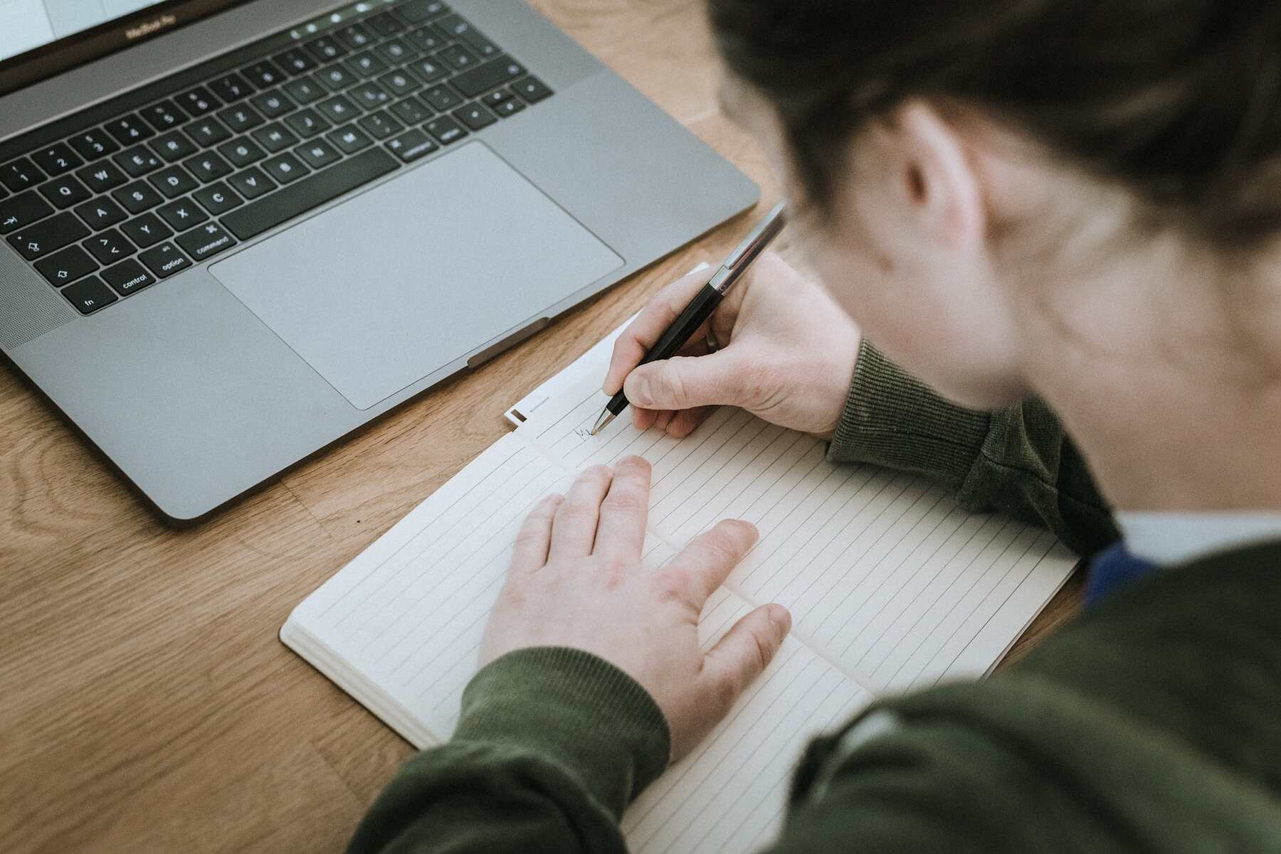 Woman writing notes while her laptop is in front of her