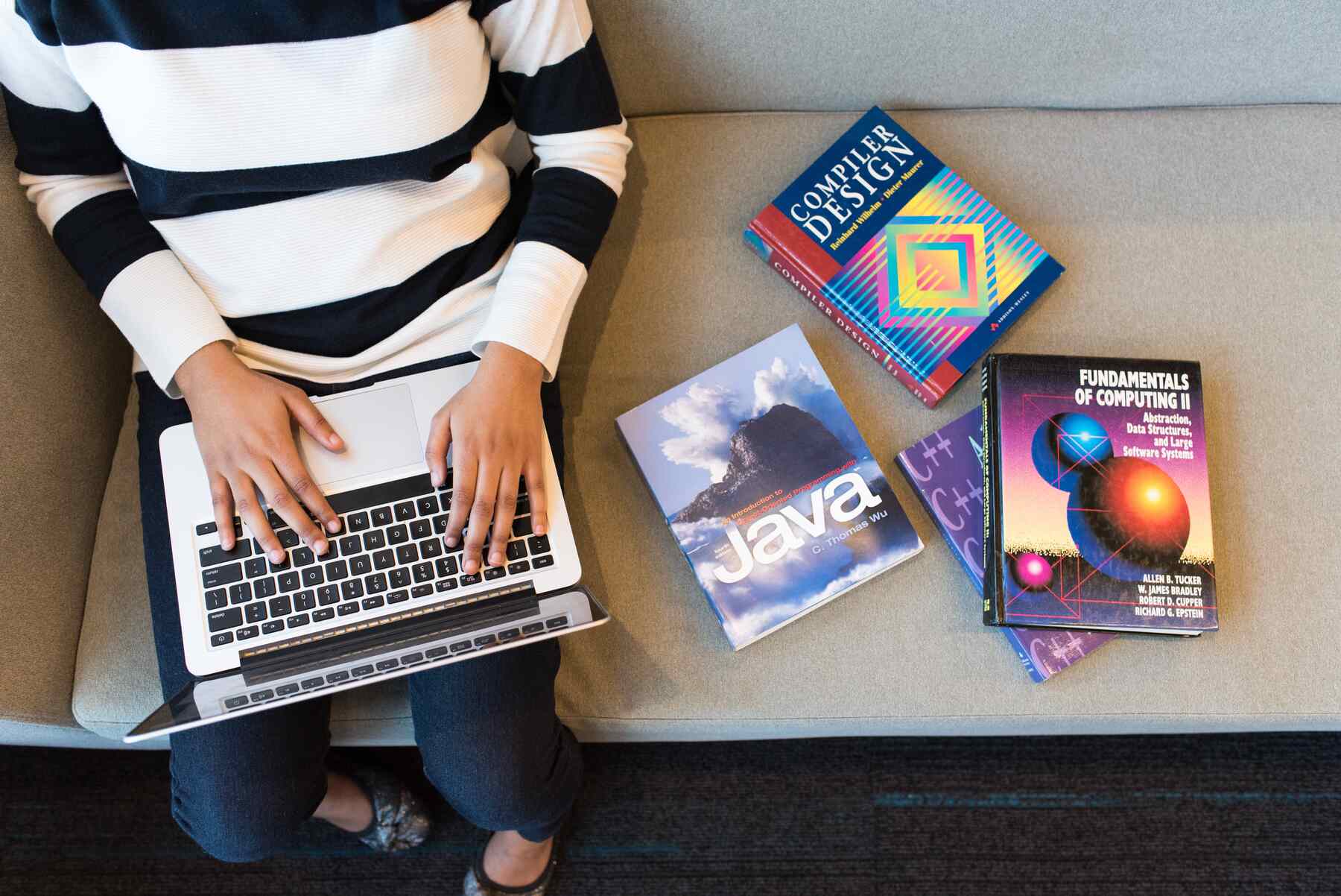 Woman using her laptop while books are piled beside her on a couch