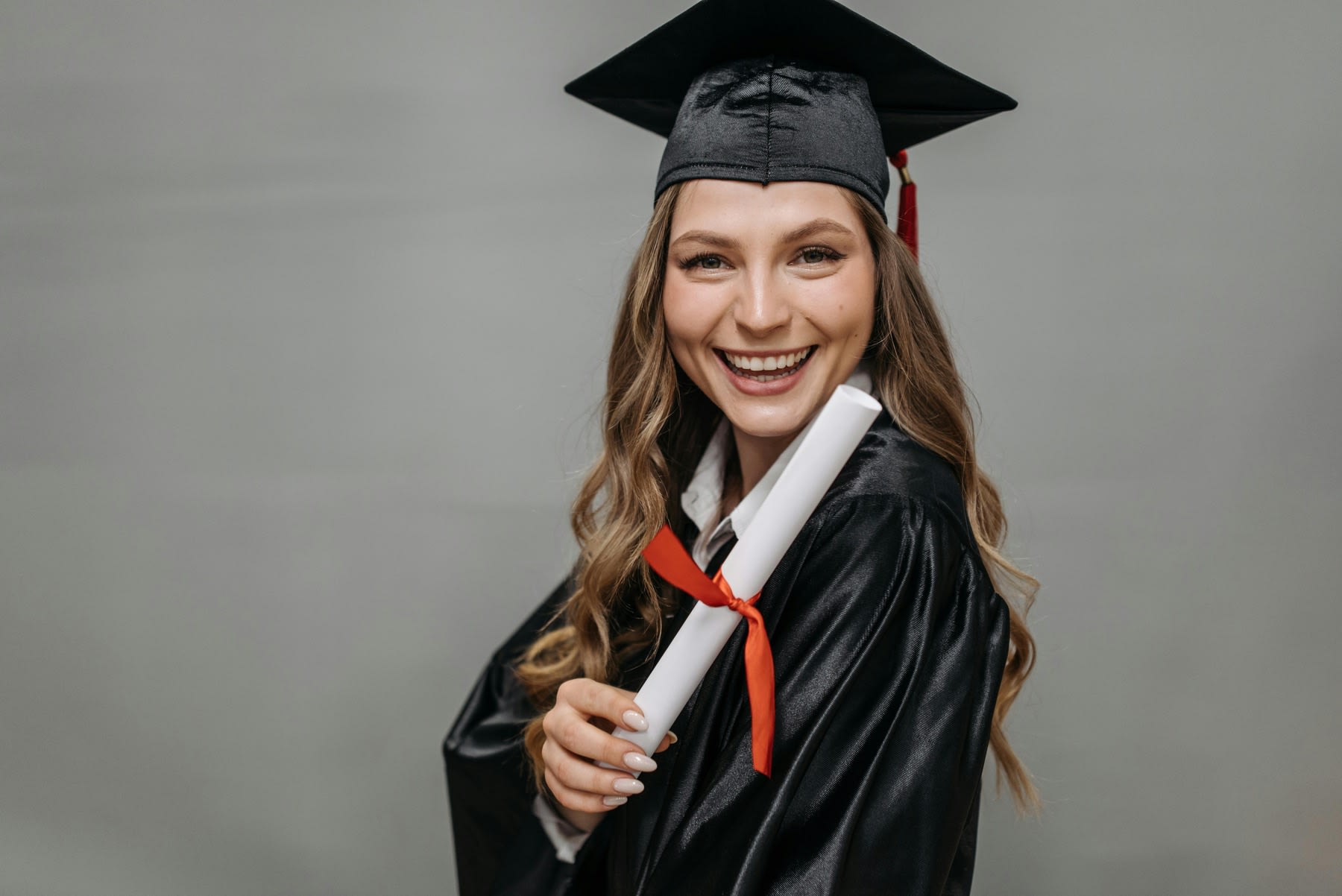 Young woman wearing graduation robes while holding her diploma